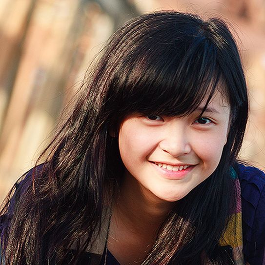 A young girl with long black hair is smiling for the camera