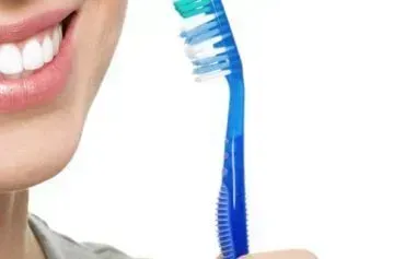 A woman is brushing her teeth with a blue toothbrush.