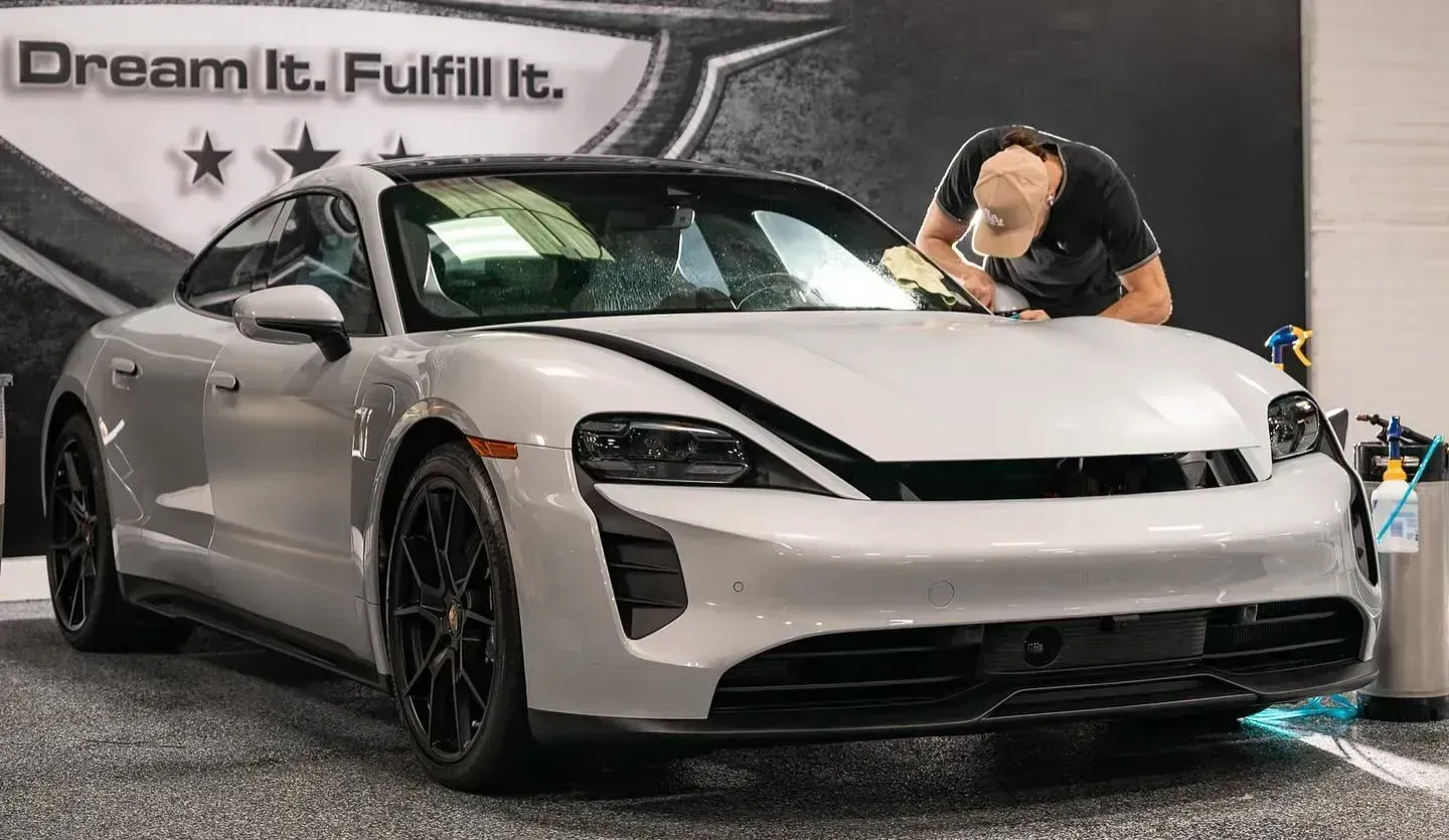 Technician carefully applying ceramic coating to a white luxury sports car to enhance paint protection and shine