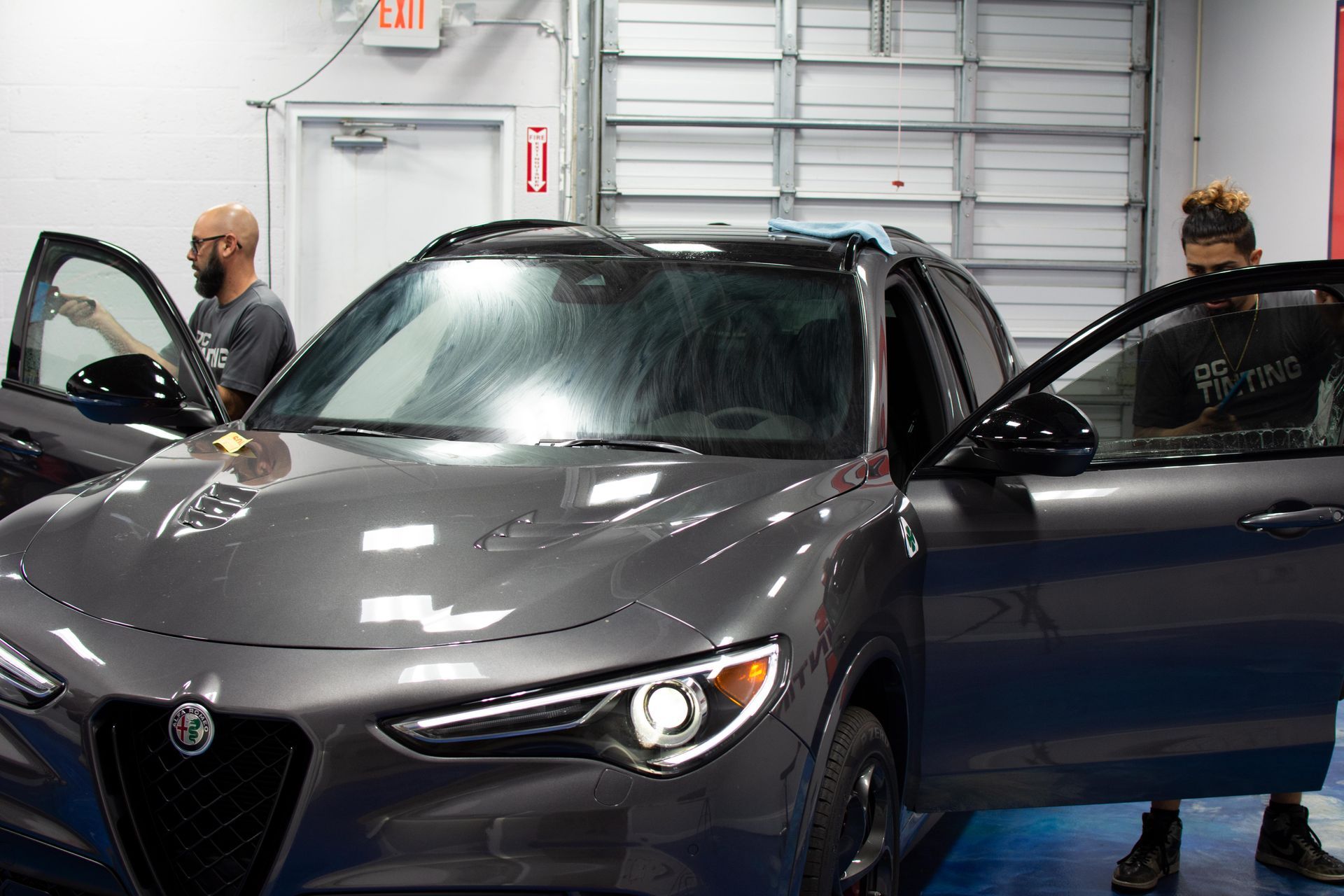 A person is tinting the windows of a gray car in a garage.