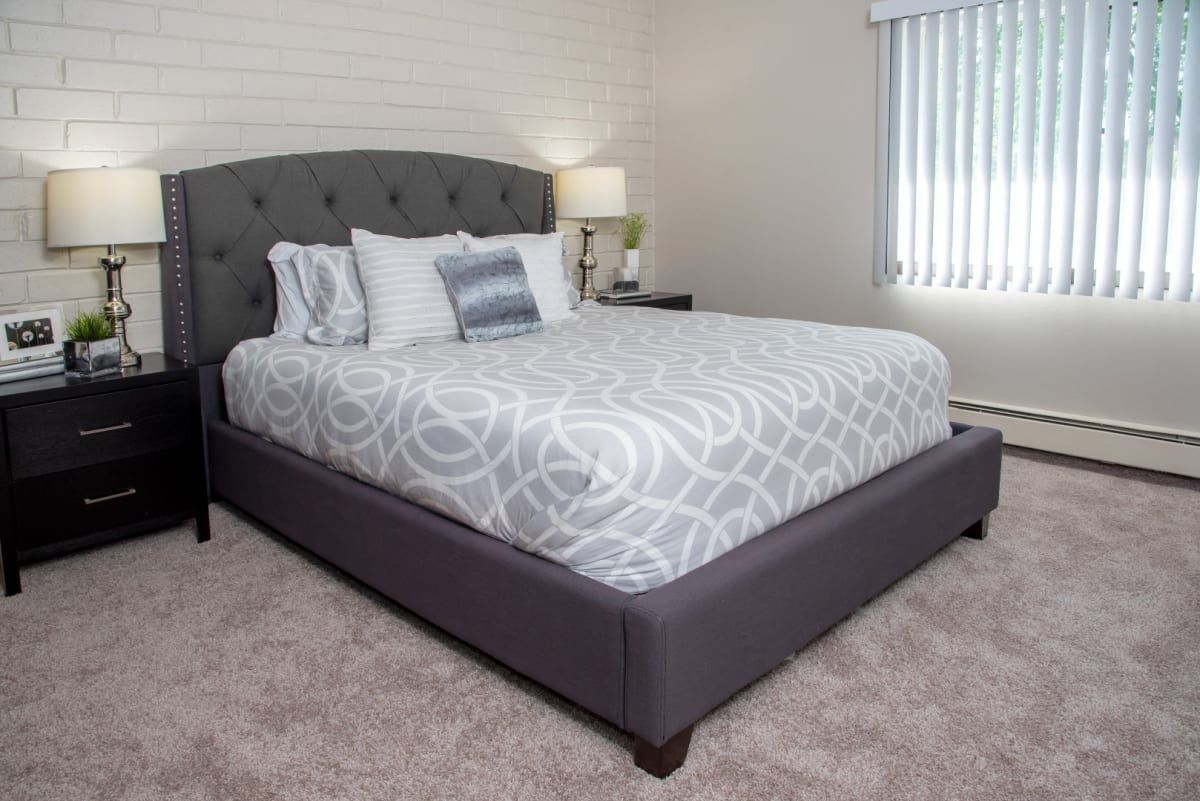 A bedroom with a bed , nightstand , lamps and a window.