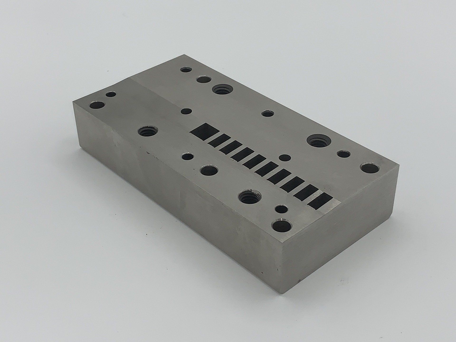 A metal block with holes in it is sitting on a white surface.