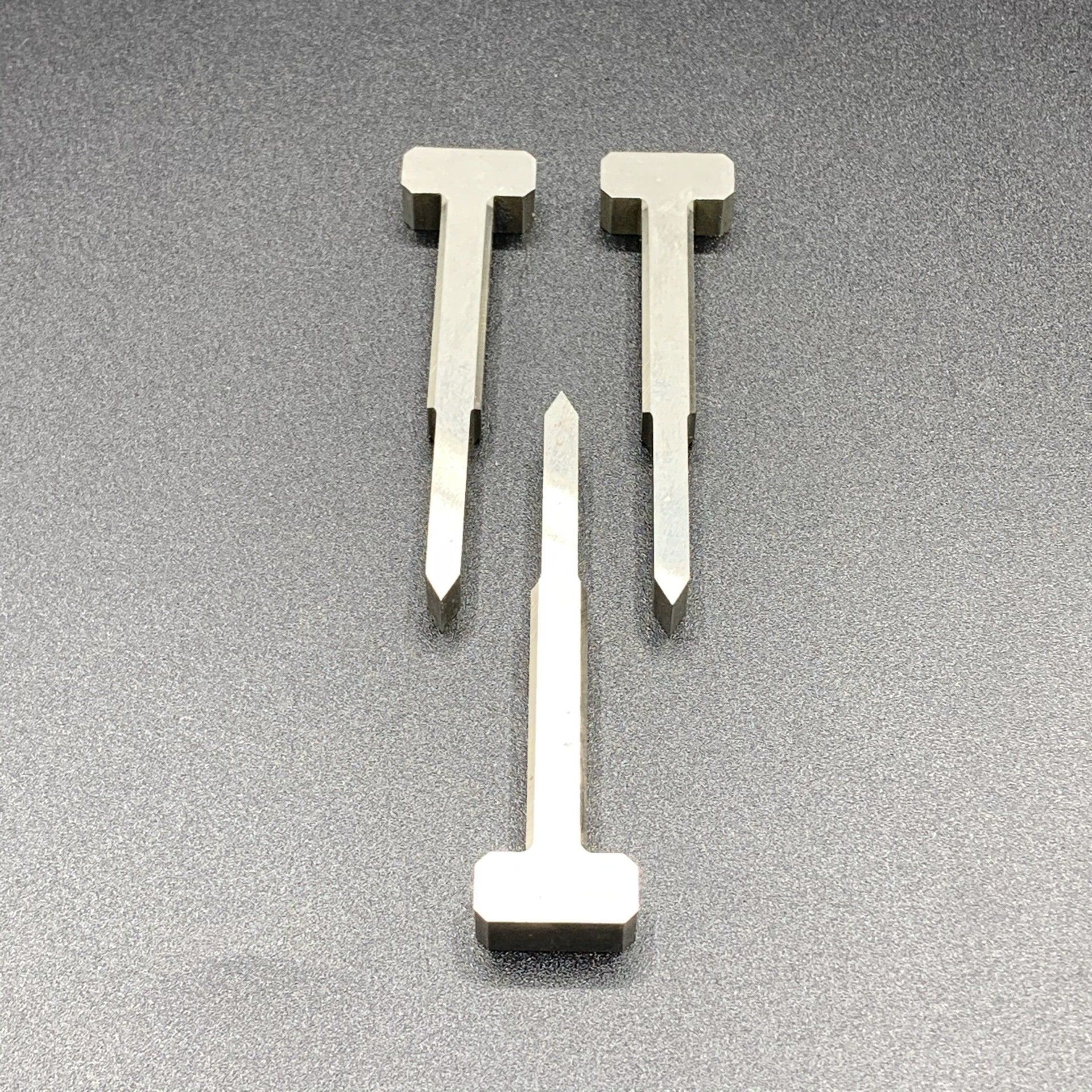 Three metal nails are sitting on a gray surface.