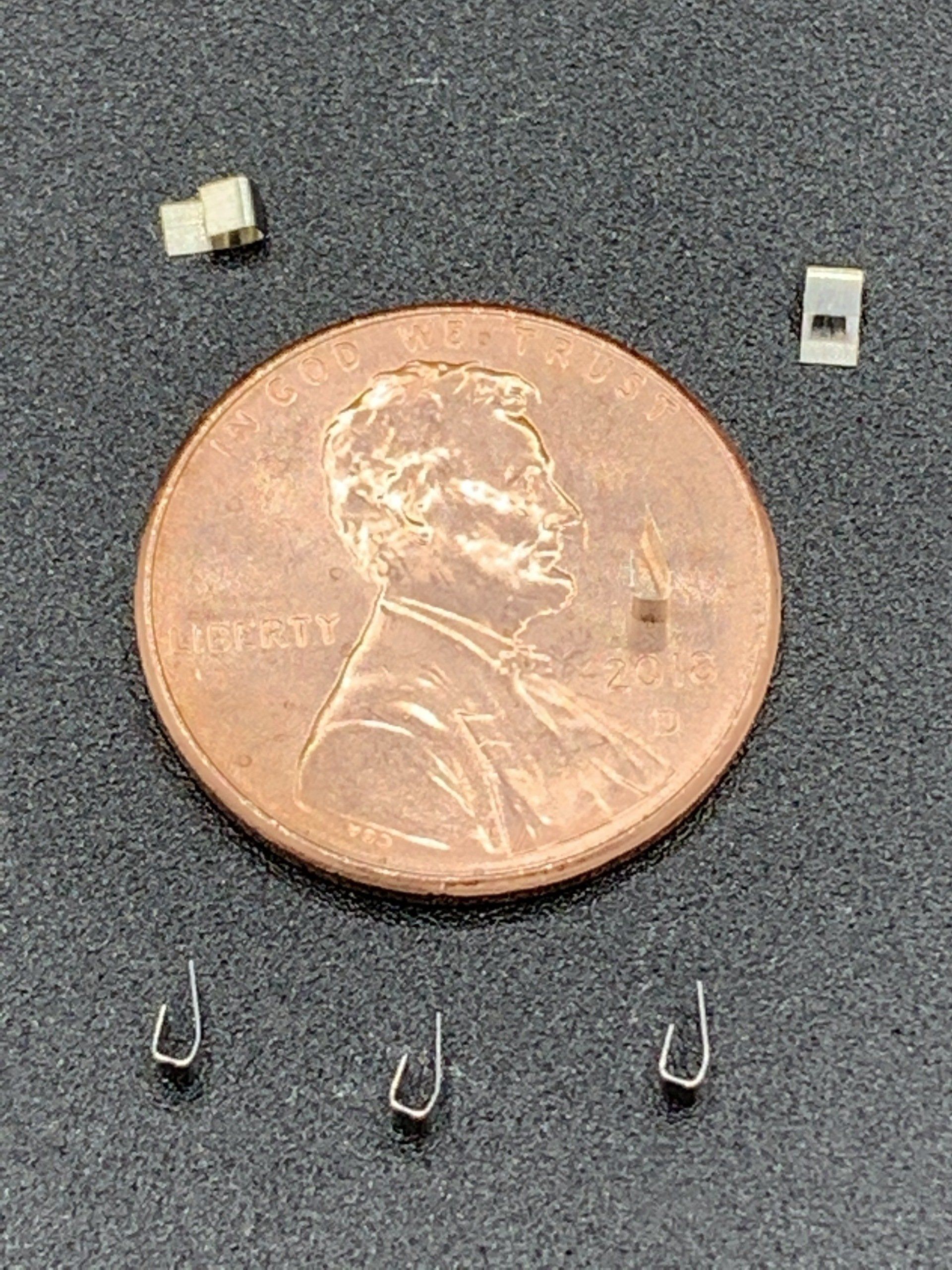 A penny is sitting on top of a table next to three hooks.