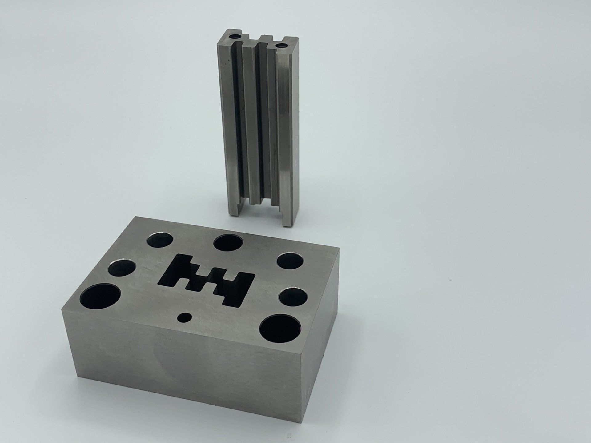 A metal block with holes in it is sitting next to a metal block with holes in it.