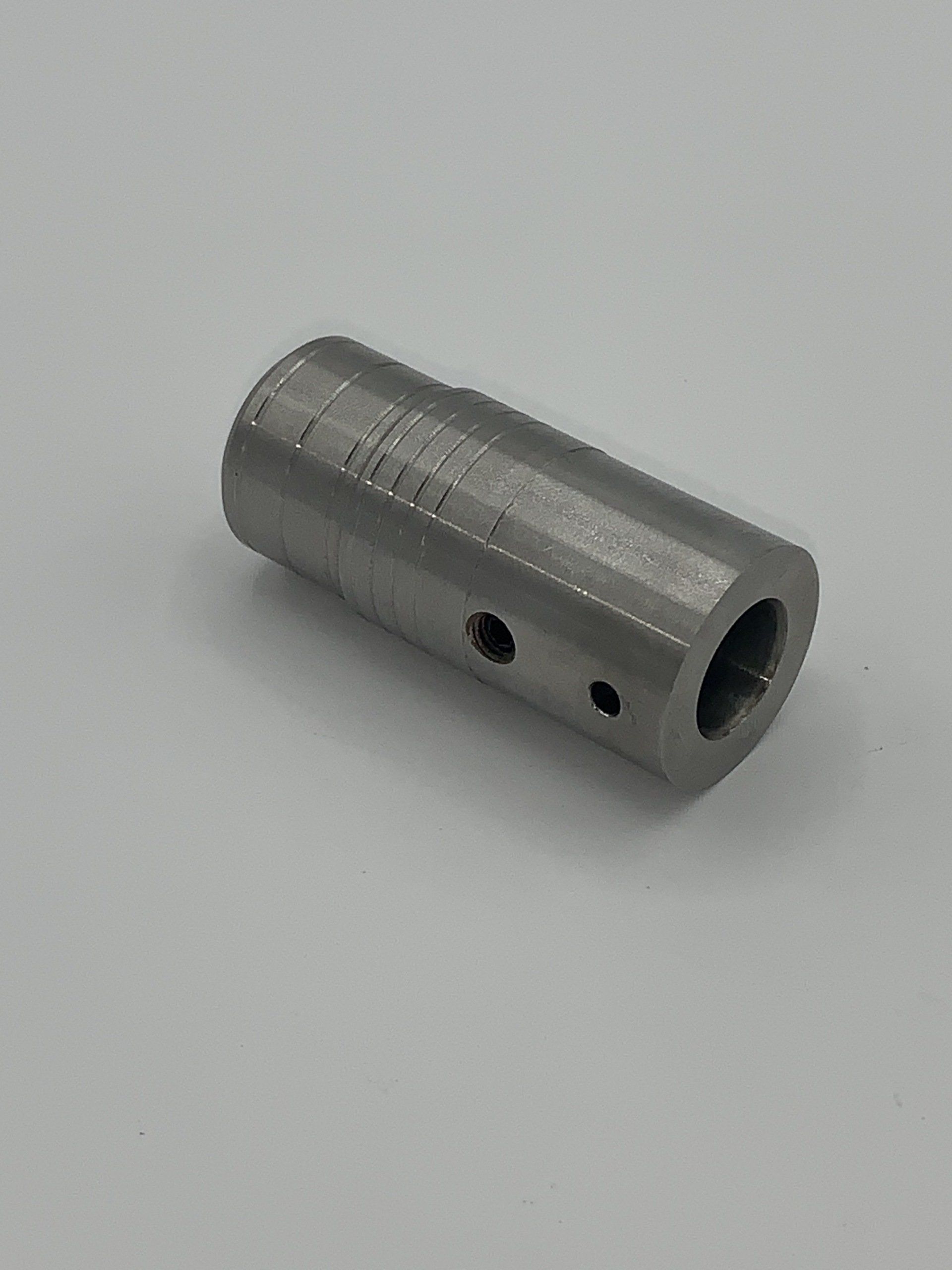 A stainless steel cylinder with two holes in it is sitting on a white surface.