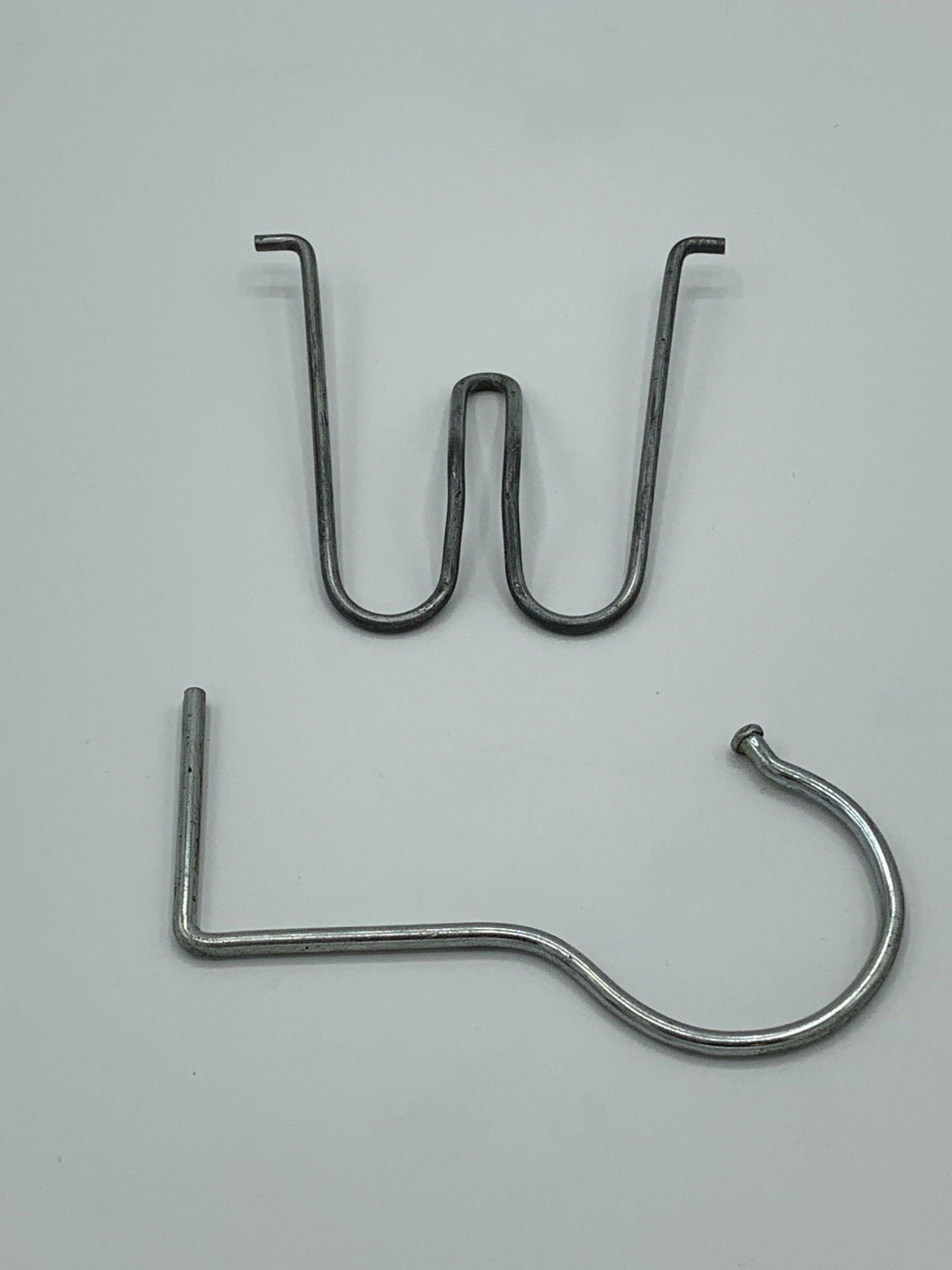 Two metal hooks are sitting on a white surface.
