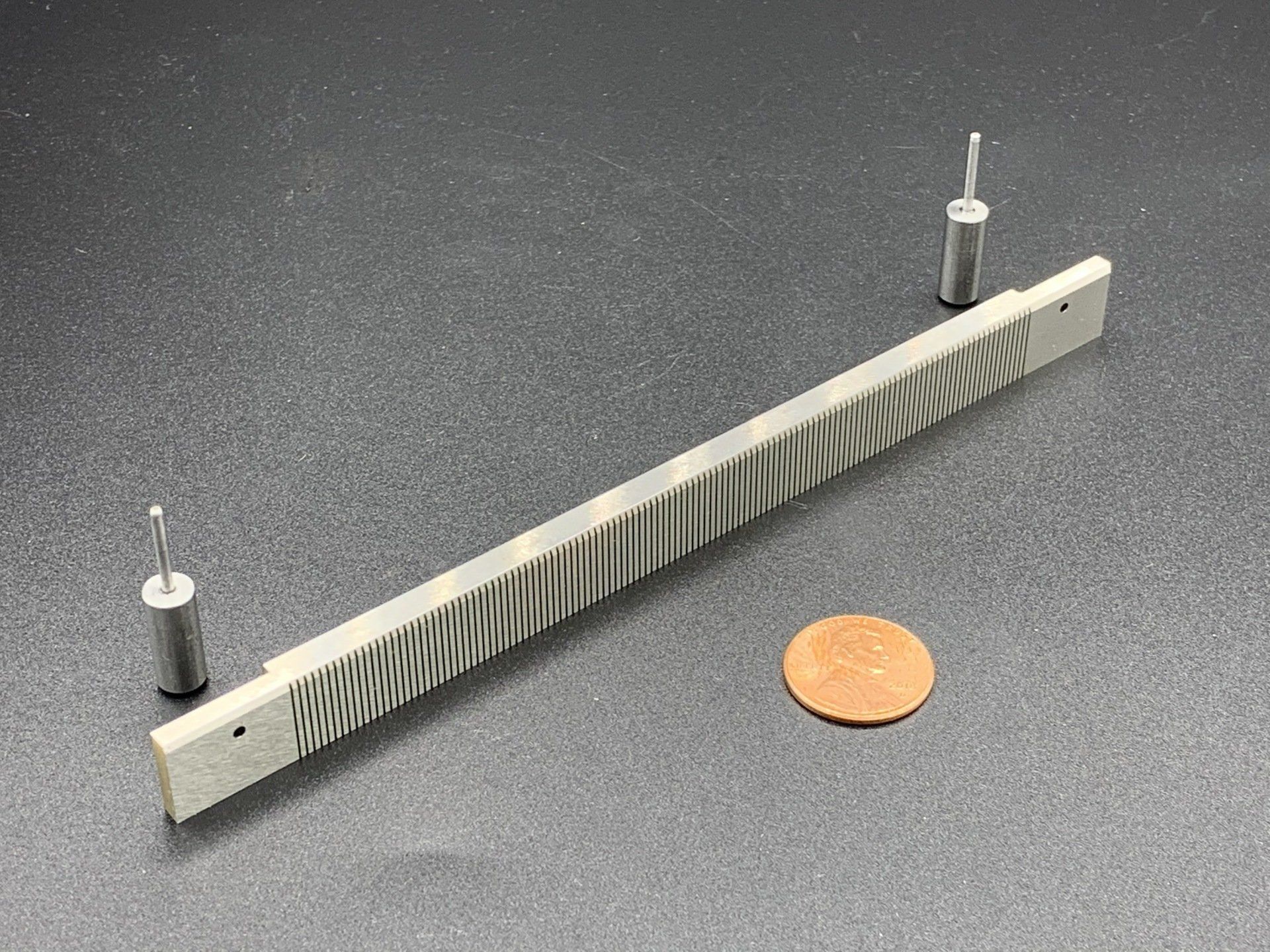 A piece of metal is sitting next to a penny on a table.