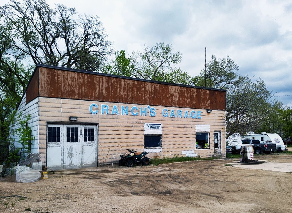 An old garage with a rusty roof is sitting in the middle of a dirt field.
