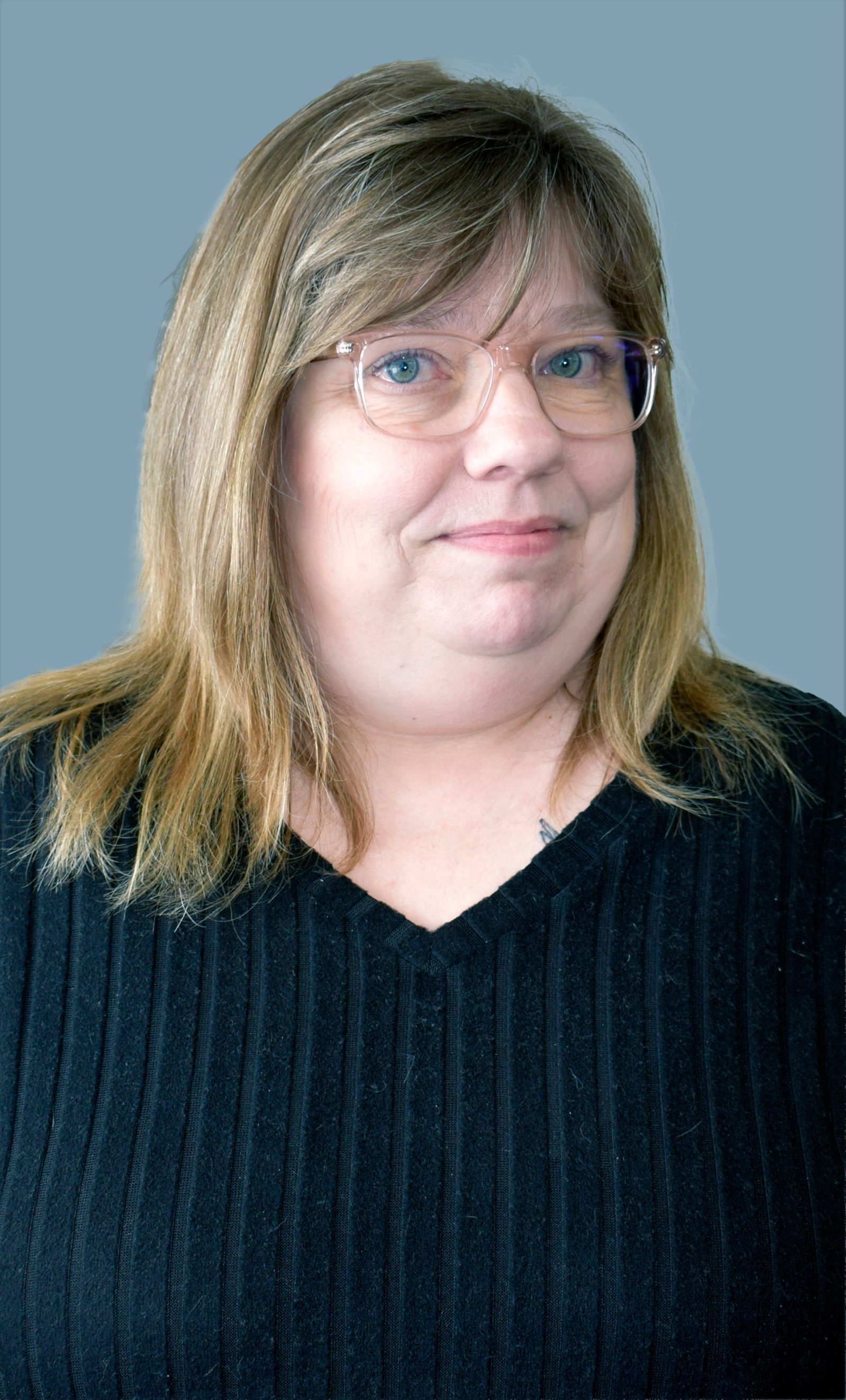 A woman wearing a pink shirt and a black and white cardigan is smiling.