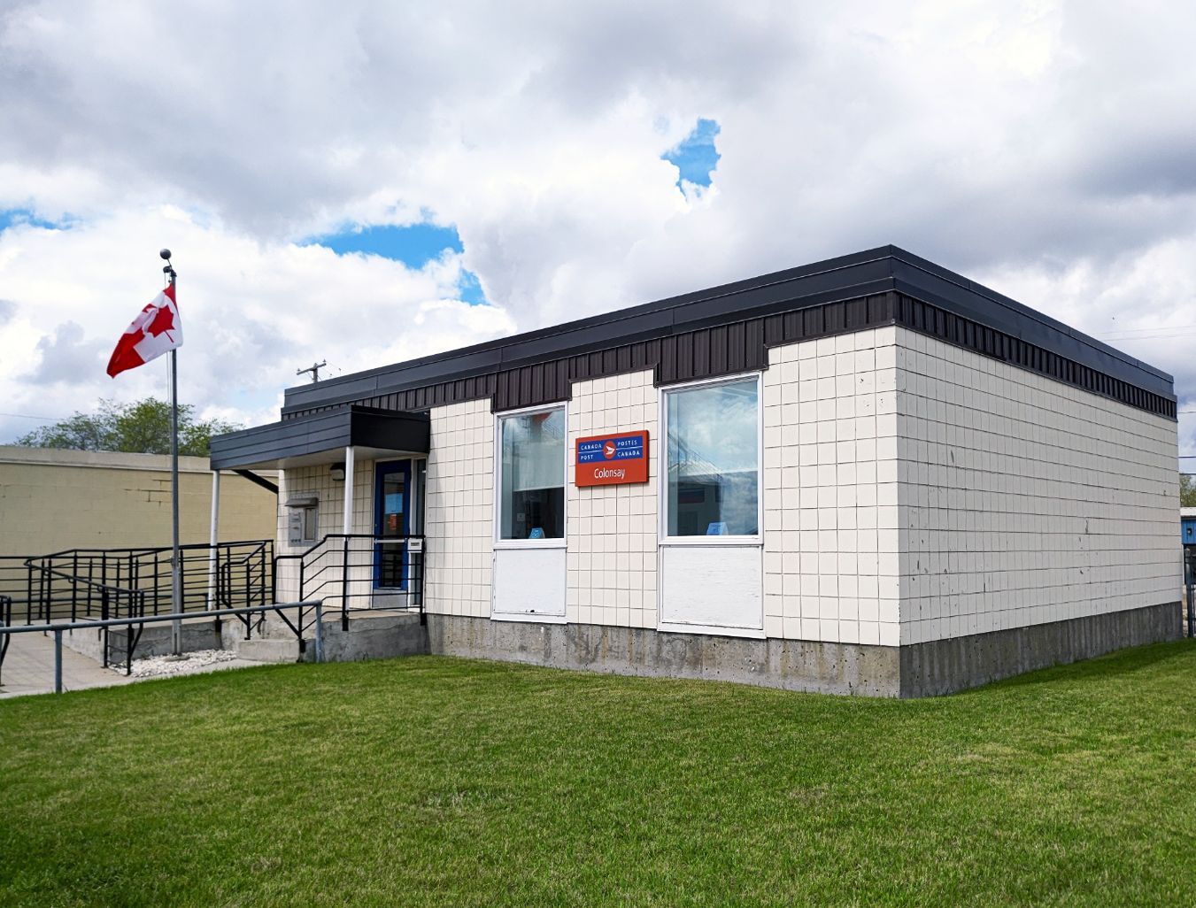 A small white building with a canadian flag flying in front of it.
