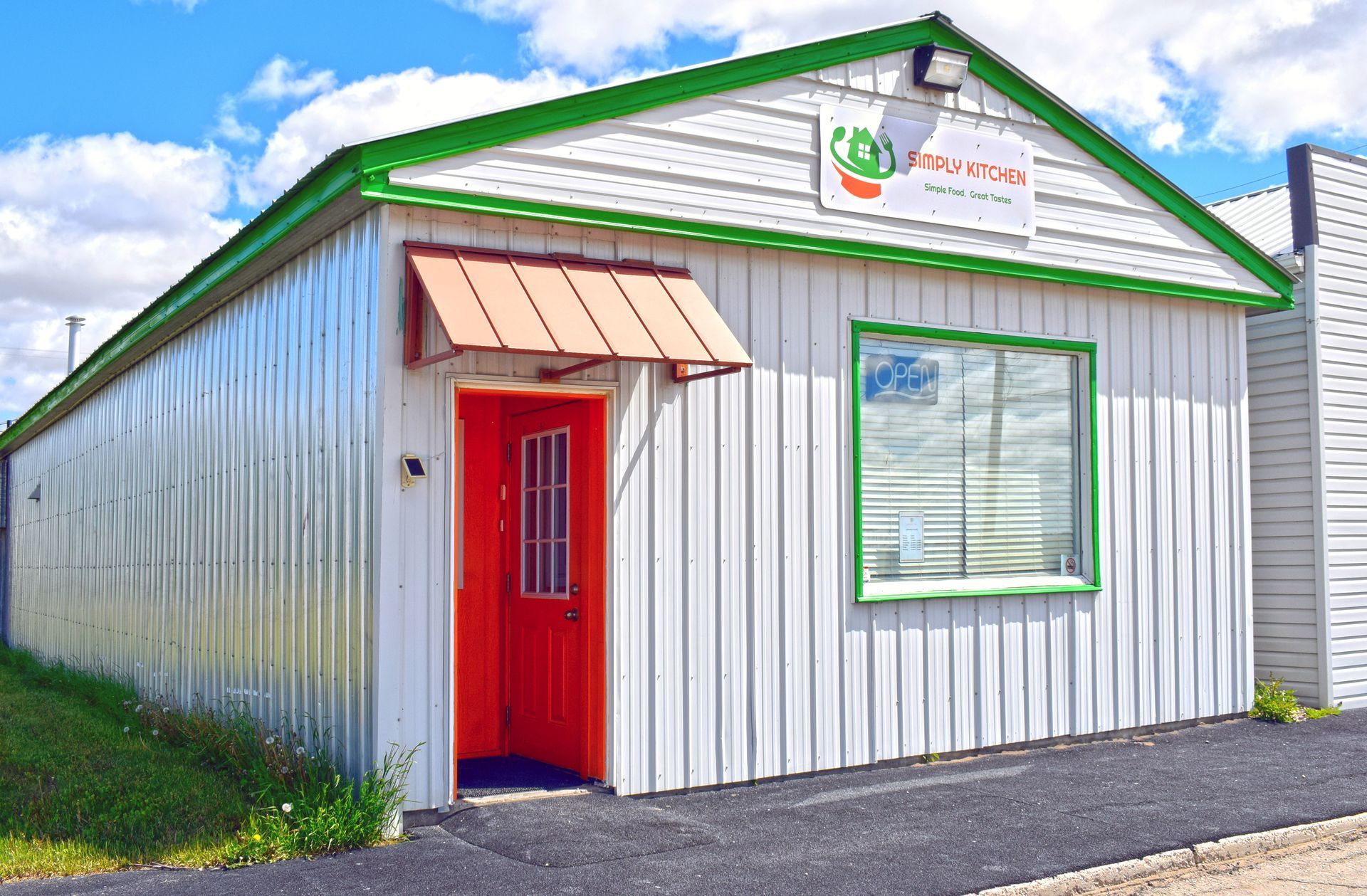 A white building with a green roof and a red door