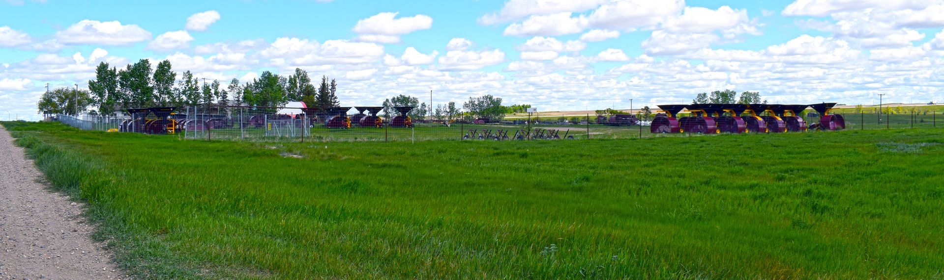 A dirt road going through a grassy field with tractors in the background.