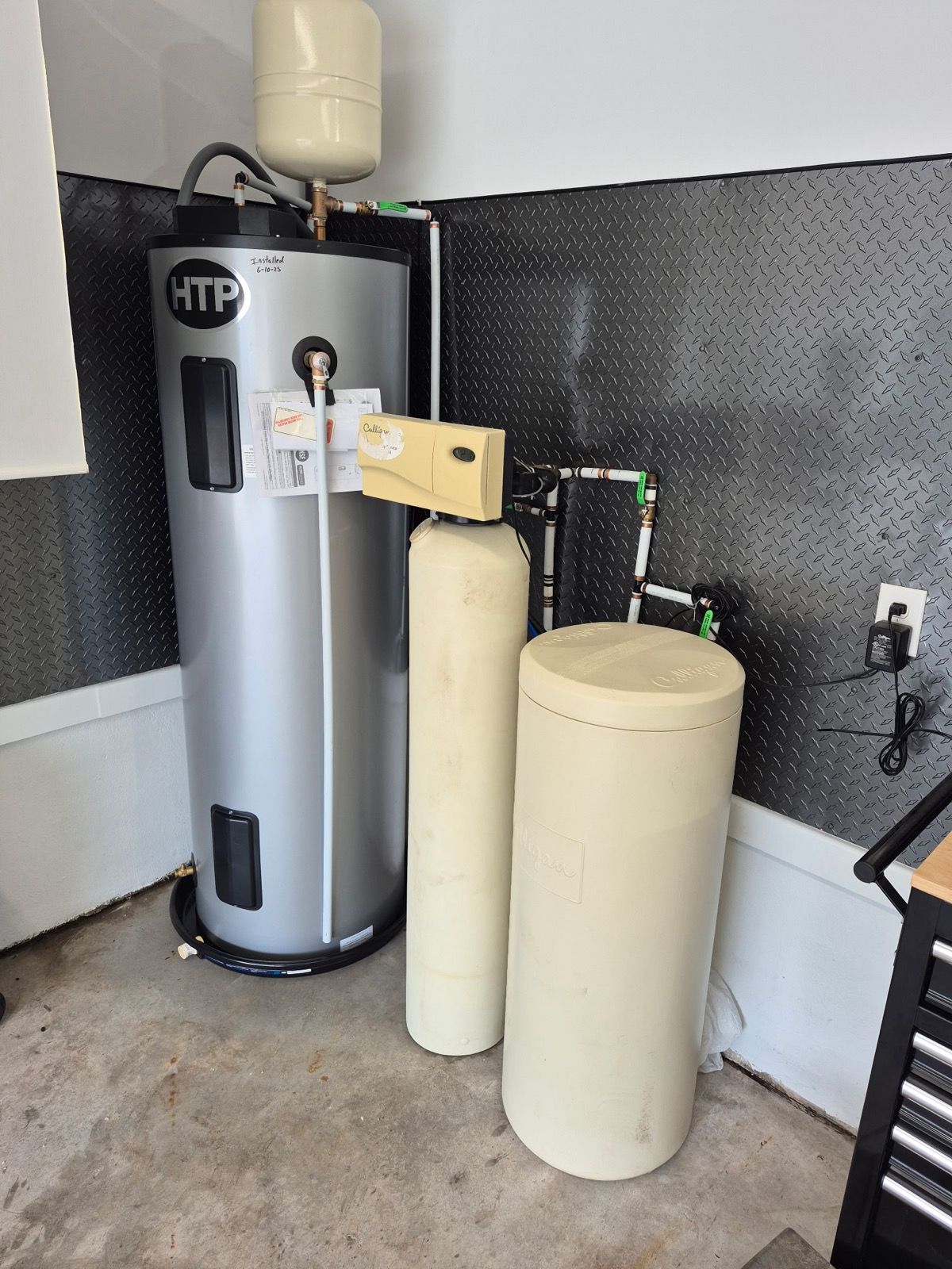 Water heater and water filtration system in a garage, with metallic silver tank and beige filter tanks.