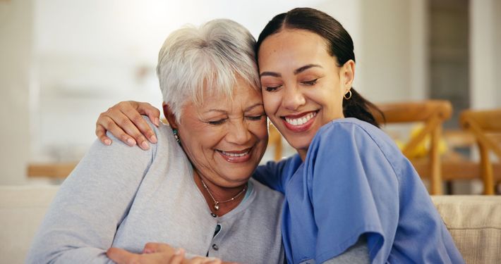 A nurse is hugging an older woman on a couch.