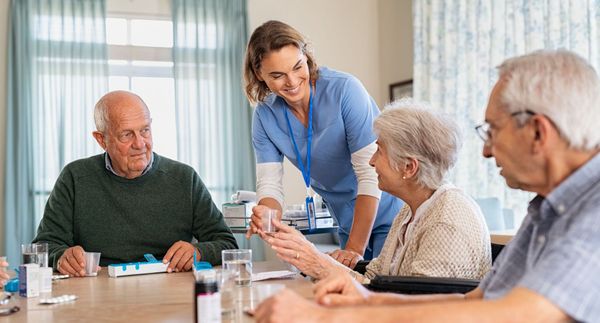 A nurse is talking to a group of elderly people sitting at a table.