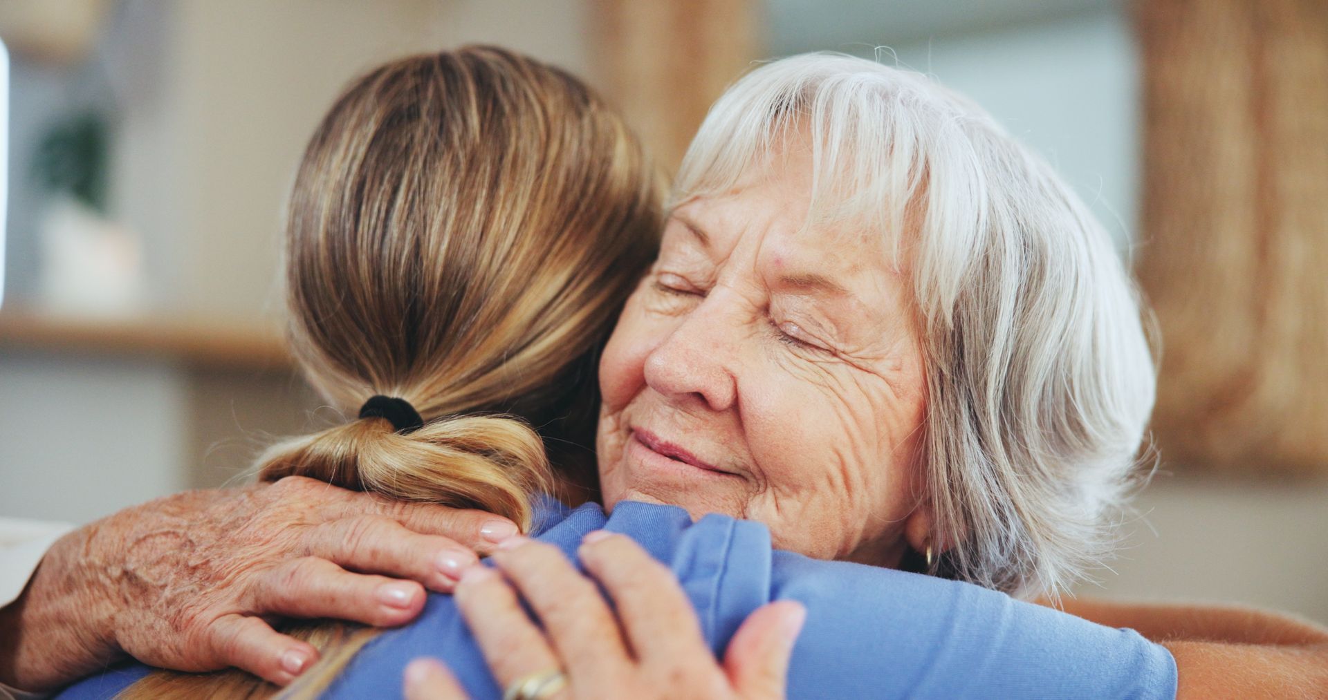 An elderly woman is hugging a younger woman.