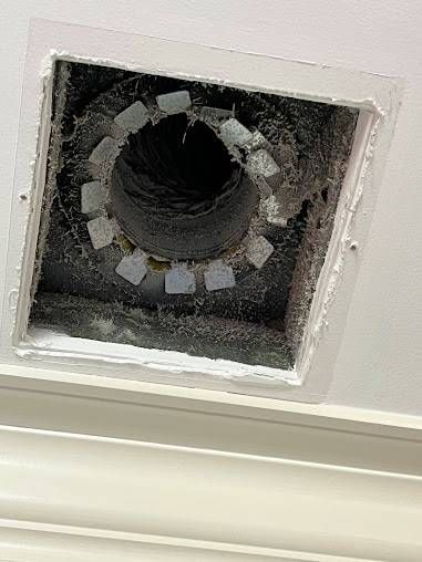 Laundry room with a dryer vent, power cord, and floor debris.