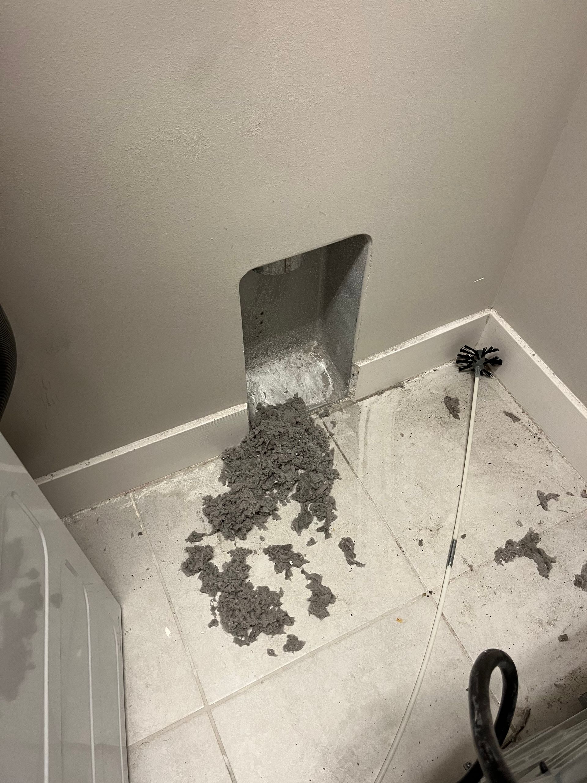 Laundry room with a dryer vent, power cord, and floor debris.