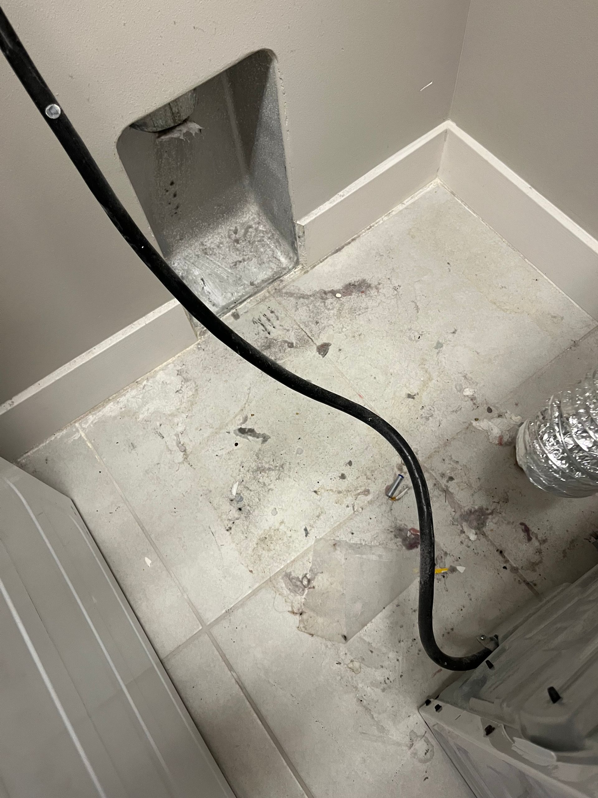 Laundry room with a dryer vent, power cord, and floor debris.