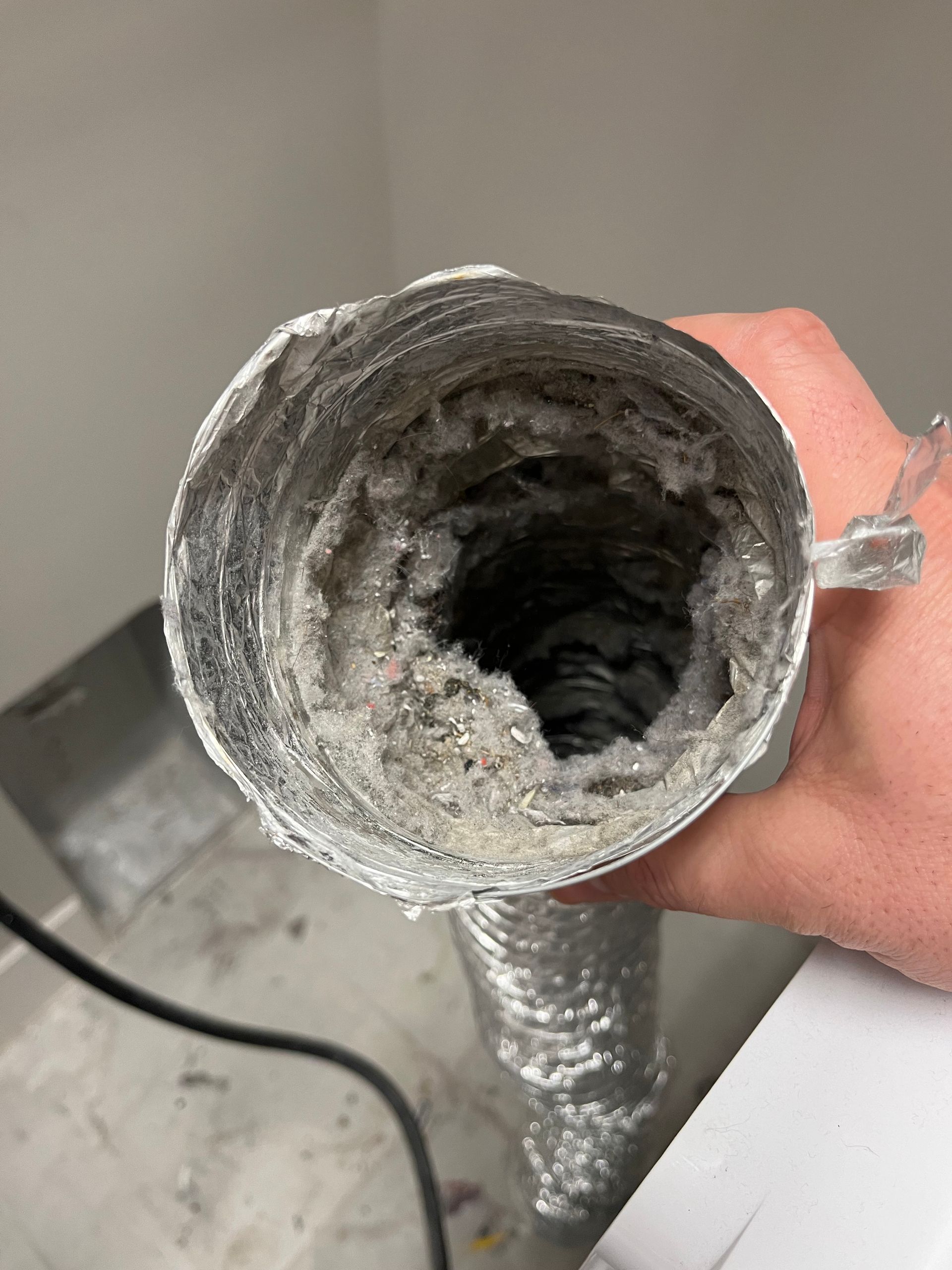 Hand holding a dirty dryer vent hose full of lint, indoors.
