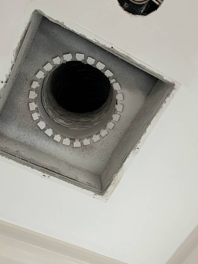 Square ceiling vent with a central black hole, surrounded by white cutouts and dusty gray interior.