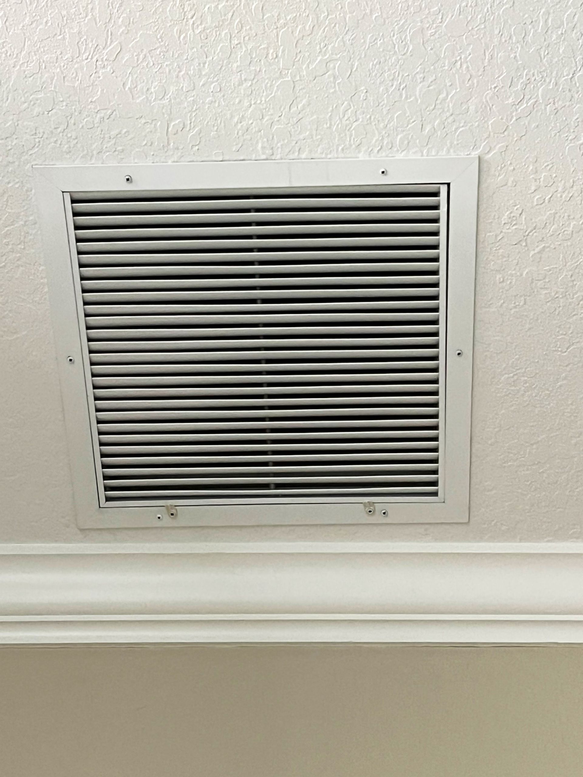 A white air vent is hanging from the ceiling of a room.