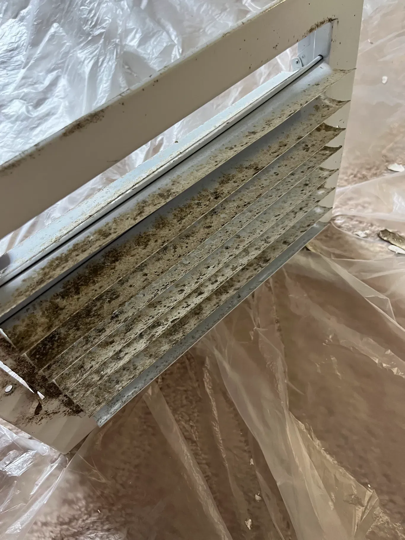 A dirty air vent is sitting on top of a plastic bag on the floor.