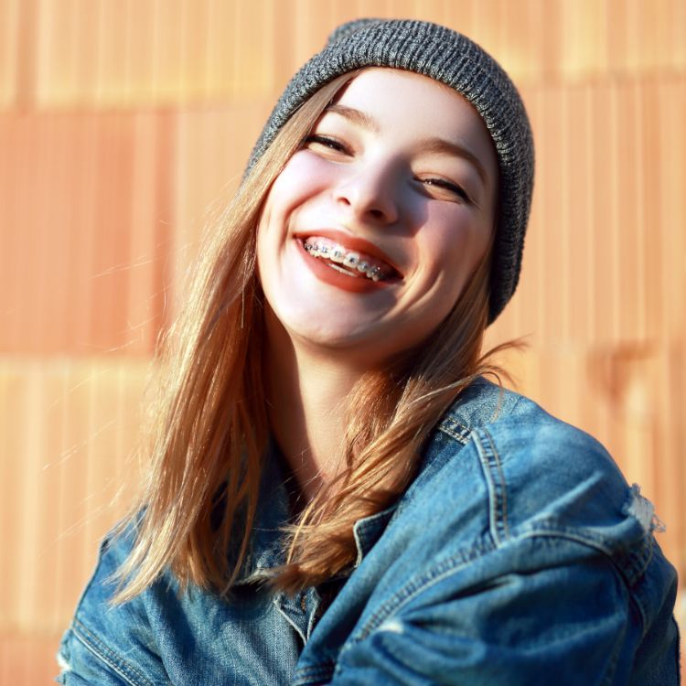 A young woman wearing braces and a beanie is smiling.