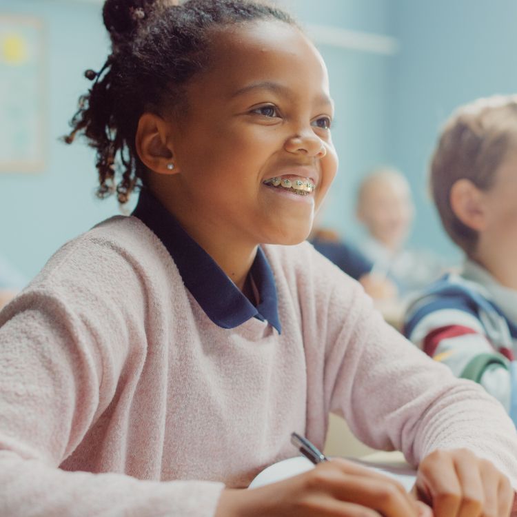 A girl in a pink sweater is smiling in a classroom