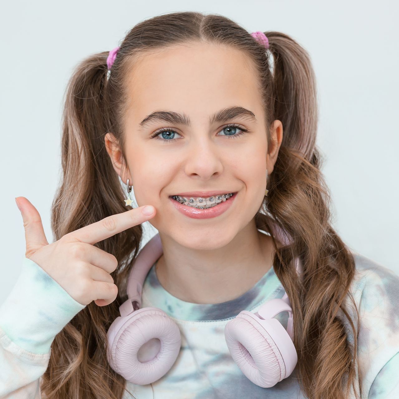 A young girl wearing braces and headphones is smiling and giving a thumbs up.