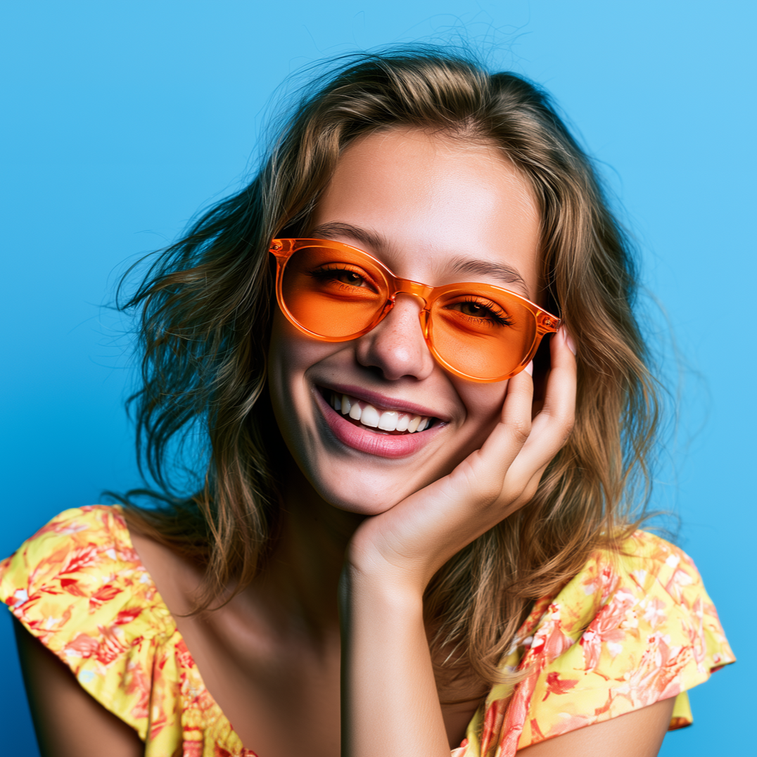 Smiling woman in orange sunglasses against a blue background, resting her face on her hand.