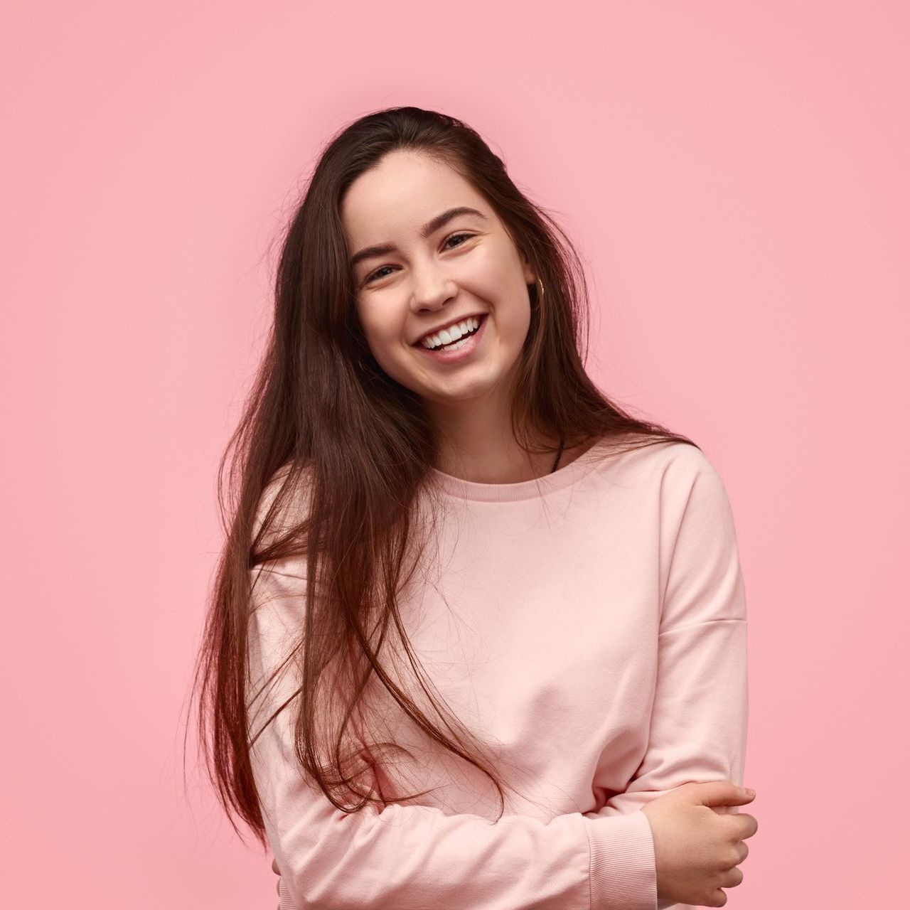 A woman in a pink sweater is smiling on a pink background.