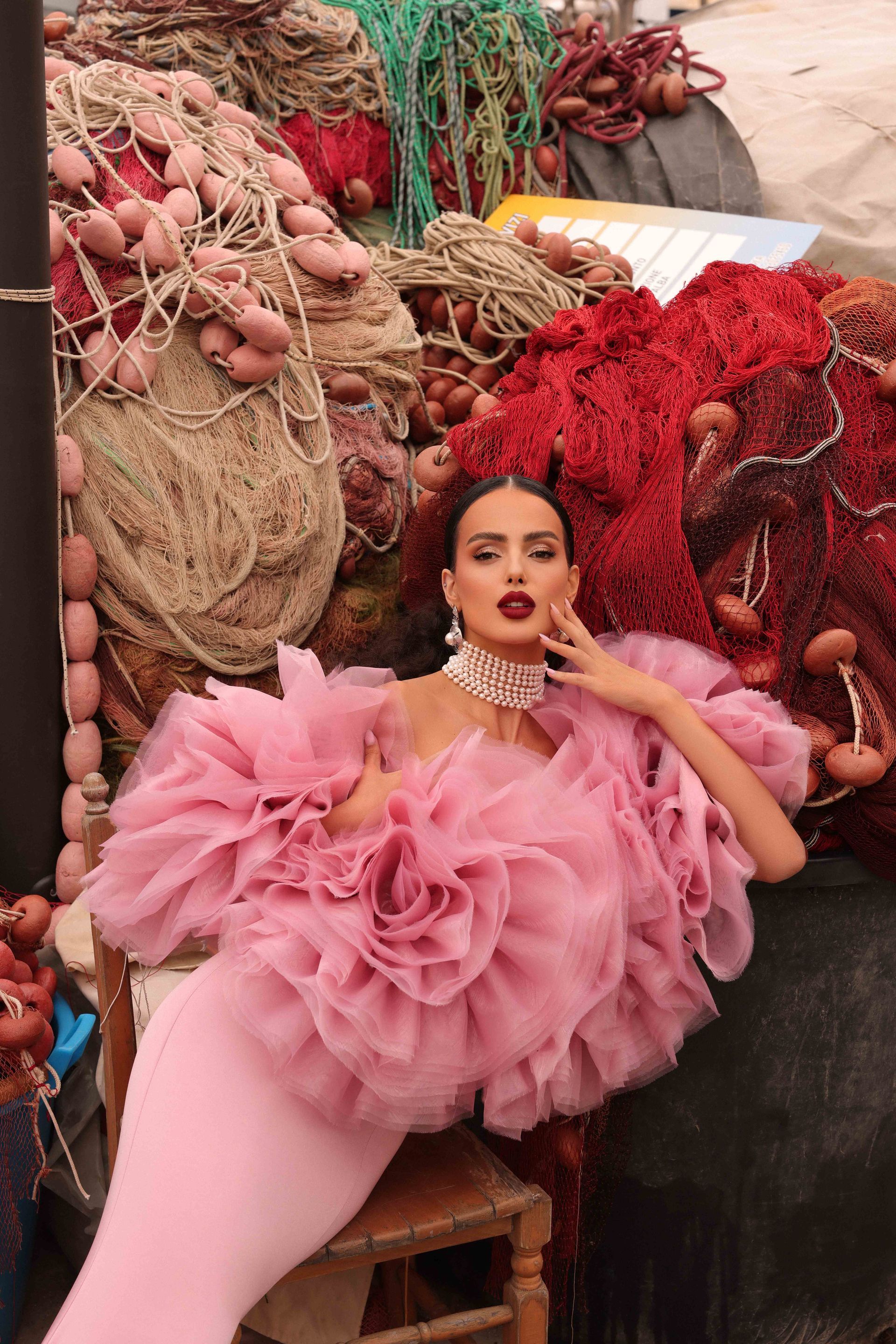 Donna in abito rosa e top a strati, in posa vicino alle reti da pesca.