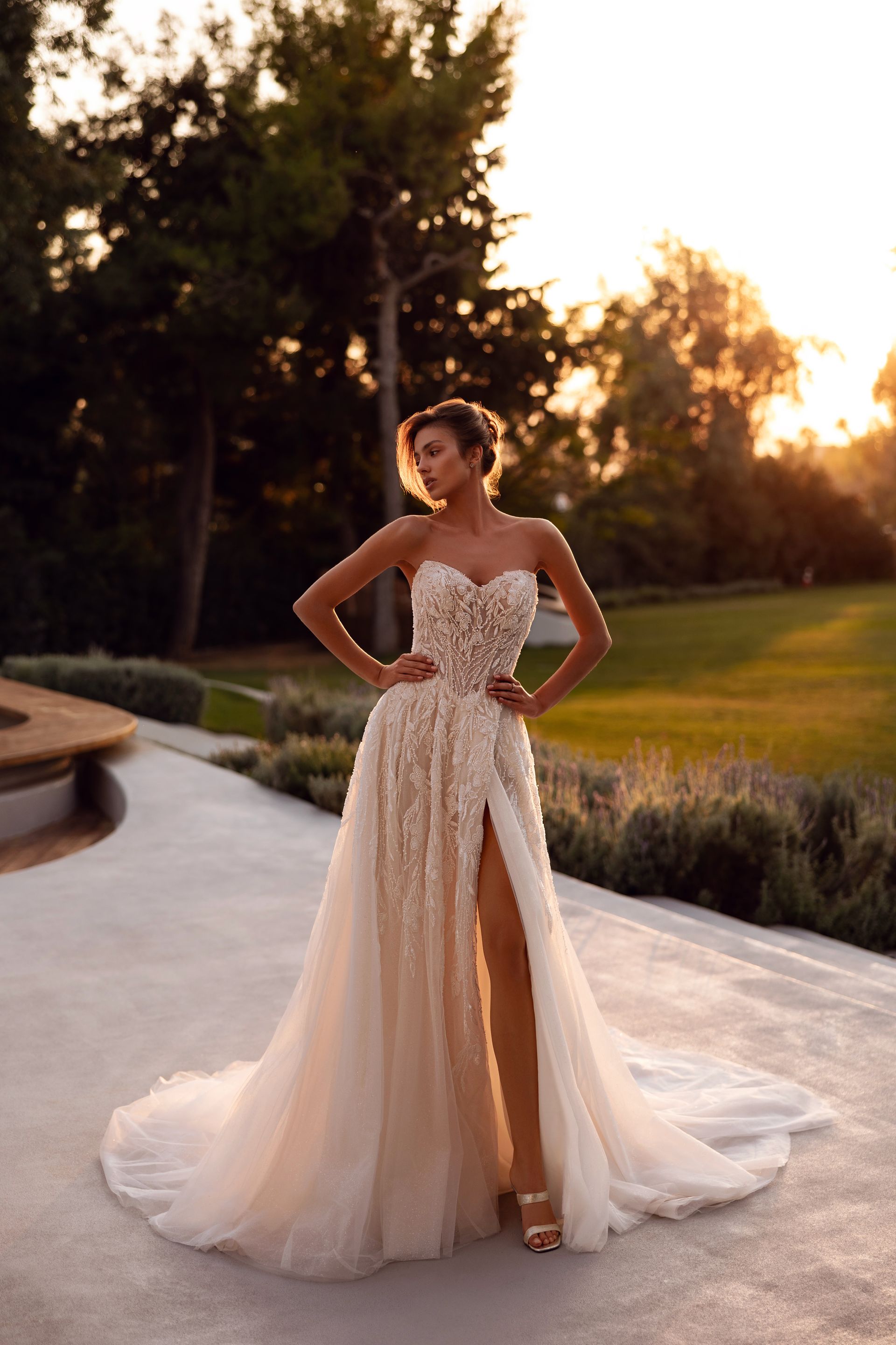 Donna in abito bianco decorato con uno spacco profondo, in piedi all'aperto al tramonto.