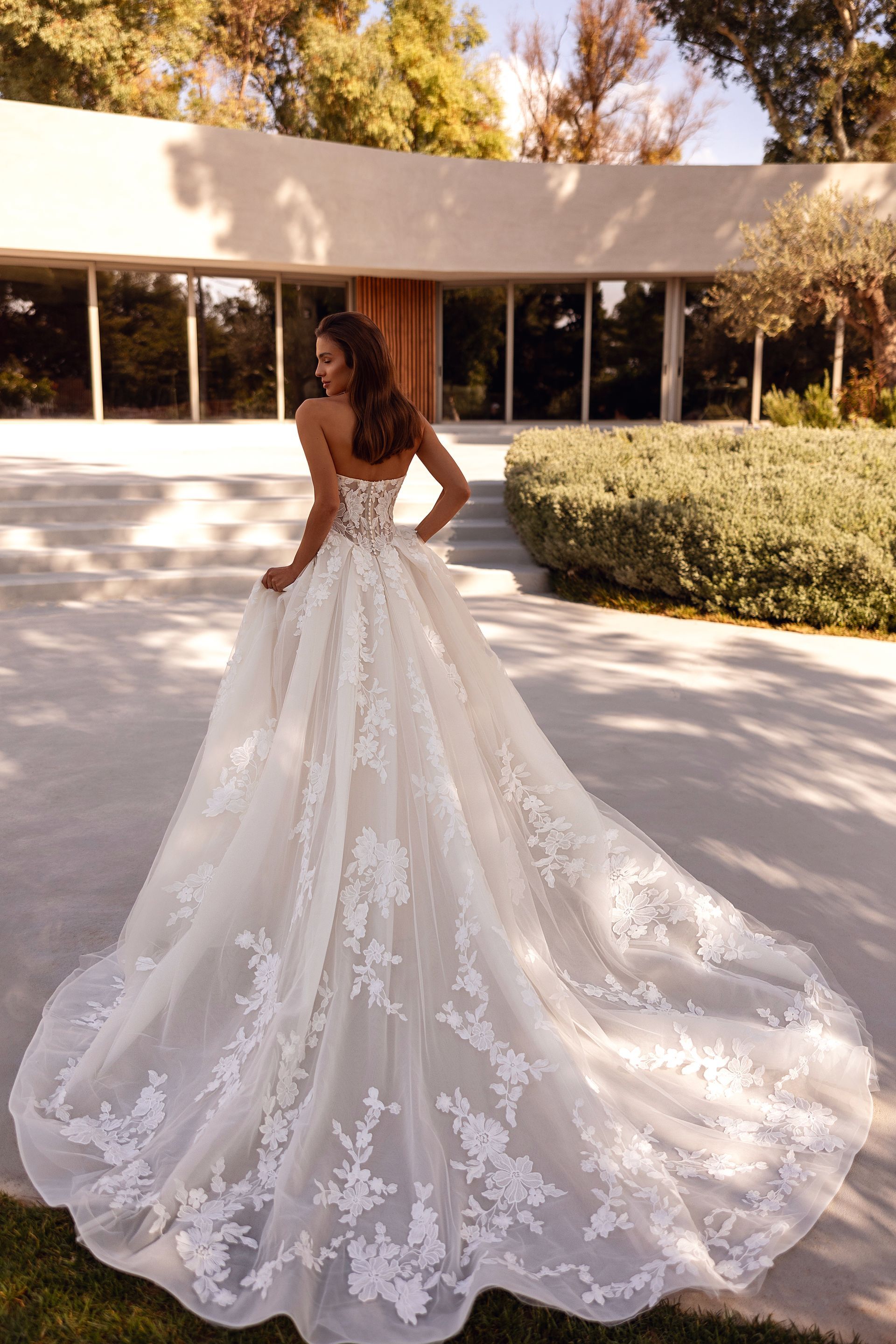 Donna in abito da sposa senza spalline con lungo strascico, in piedi fuori da un edificio.