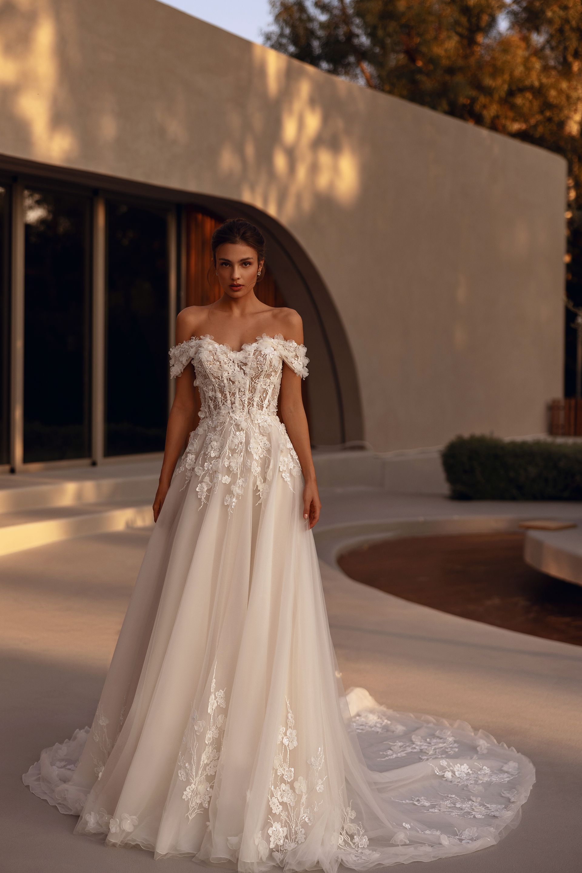 Donna in abito da sposa floreale con spalle scoperte, in posa all'aperto di fronte a un edificio moderno