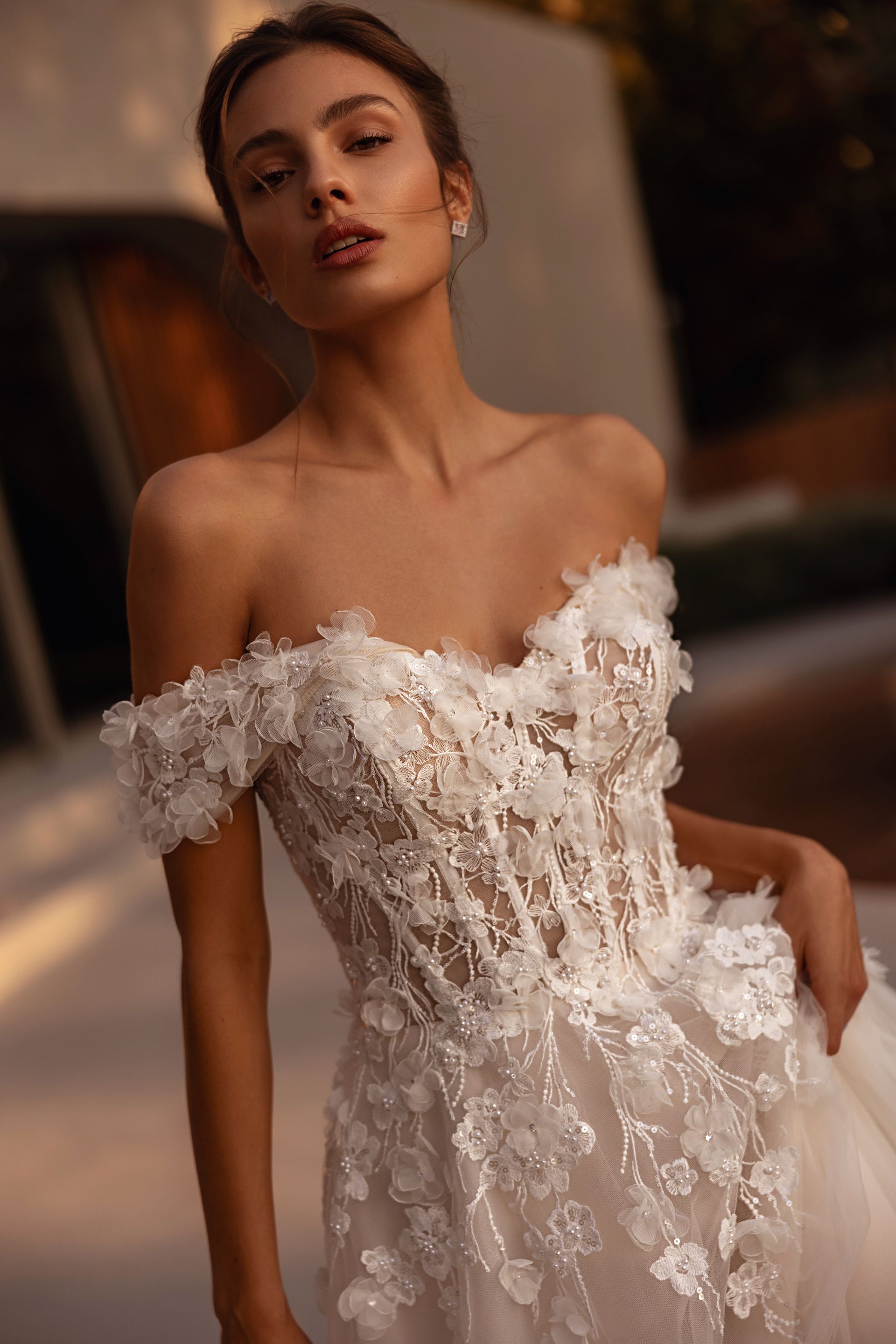 Donna in abito da sposa in pizzo floreale con spalle scoperte, luce naturale.