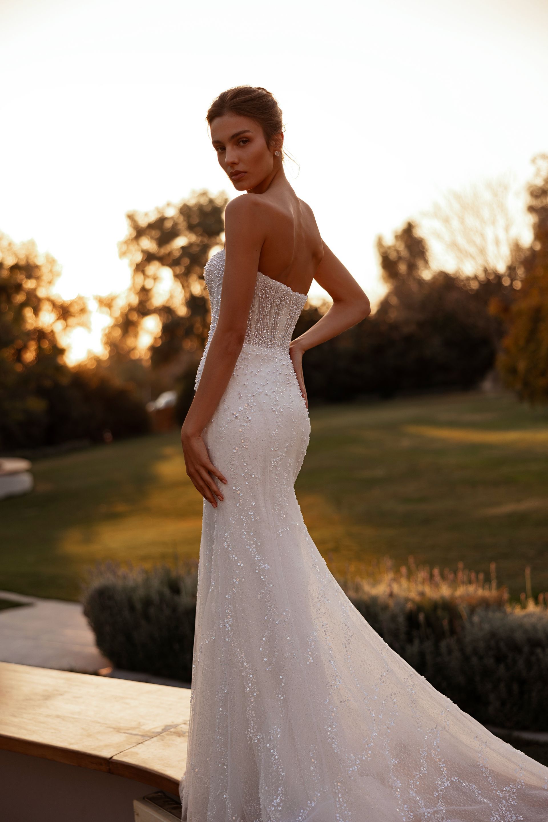 Donna in abito da sposa senza spalline decorato con perline, in posa all'aperto con un lungo strascico.