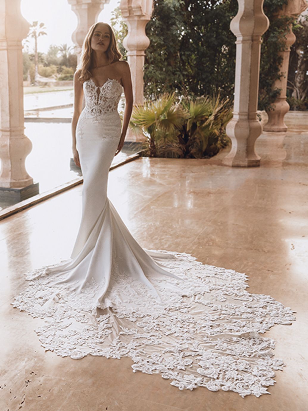 Donna in un abito da sposa bianco senza spalline in stile sirena con un lungo strascico in pizzo decorato