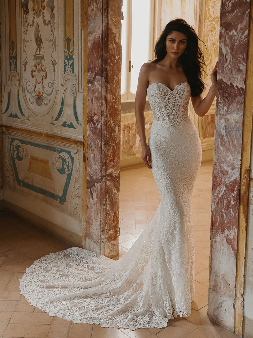 Donna con abito da sposa bianco senza spalline in pizzo, in piedi su un portone con un lungo strascico