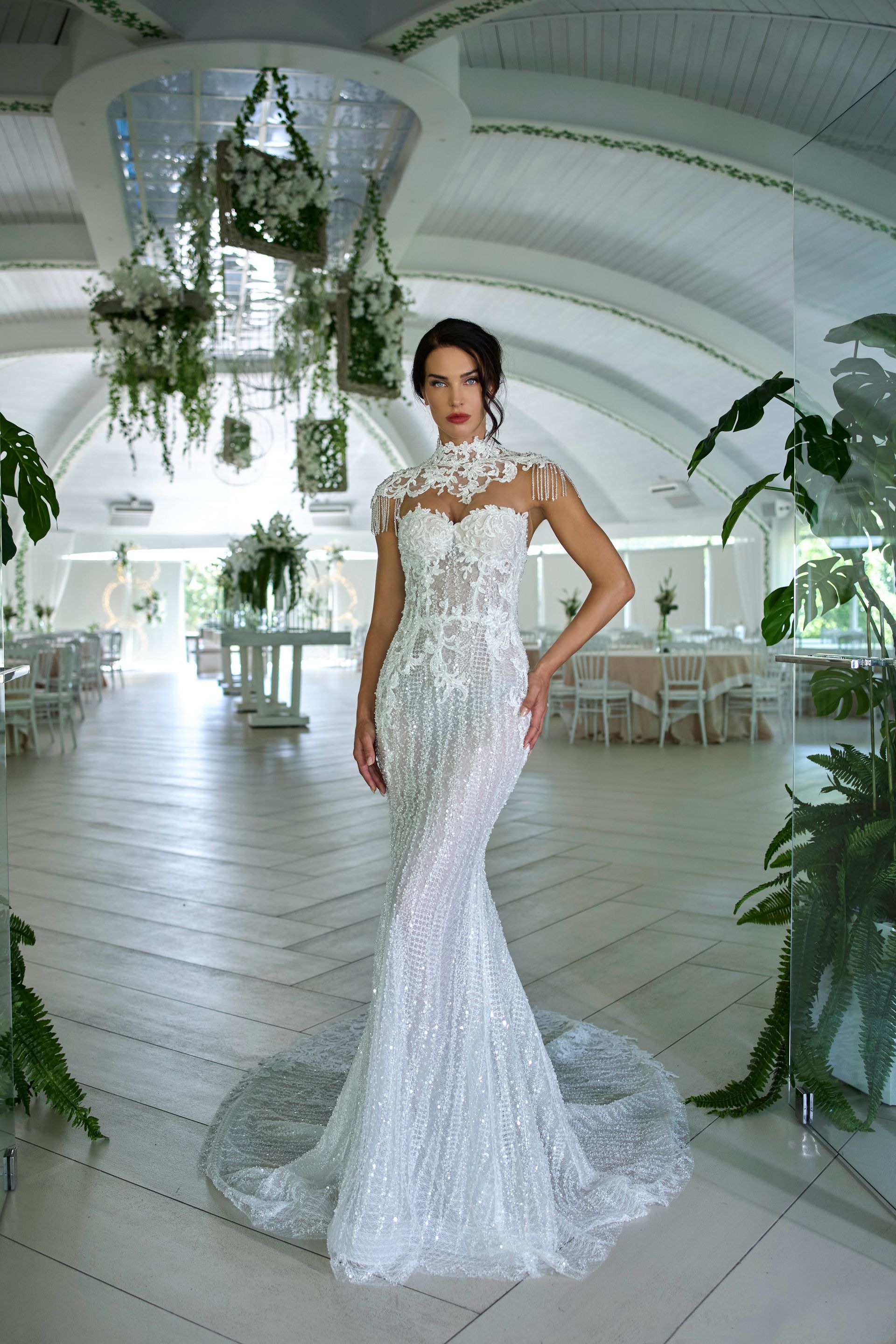 Donna in abito da sposa bianco con perline in una location luminosa con decorazioni floreali appese.