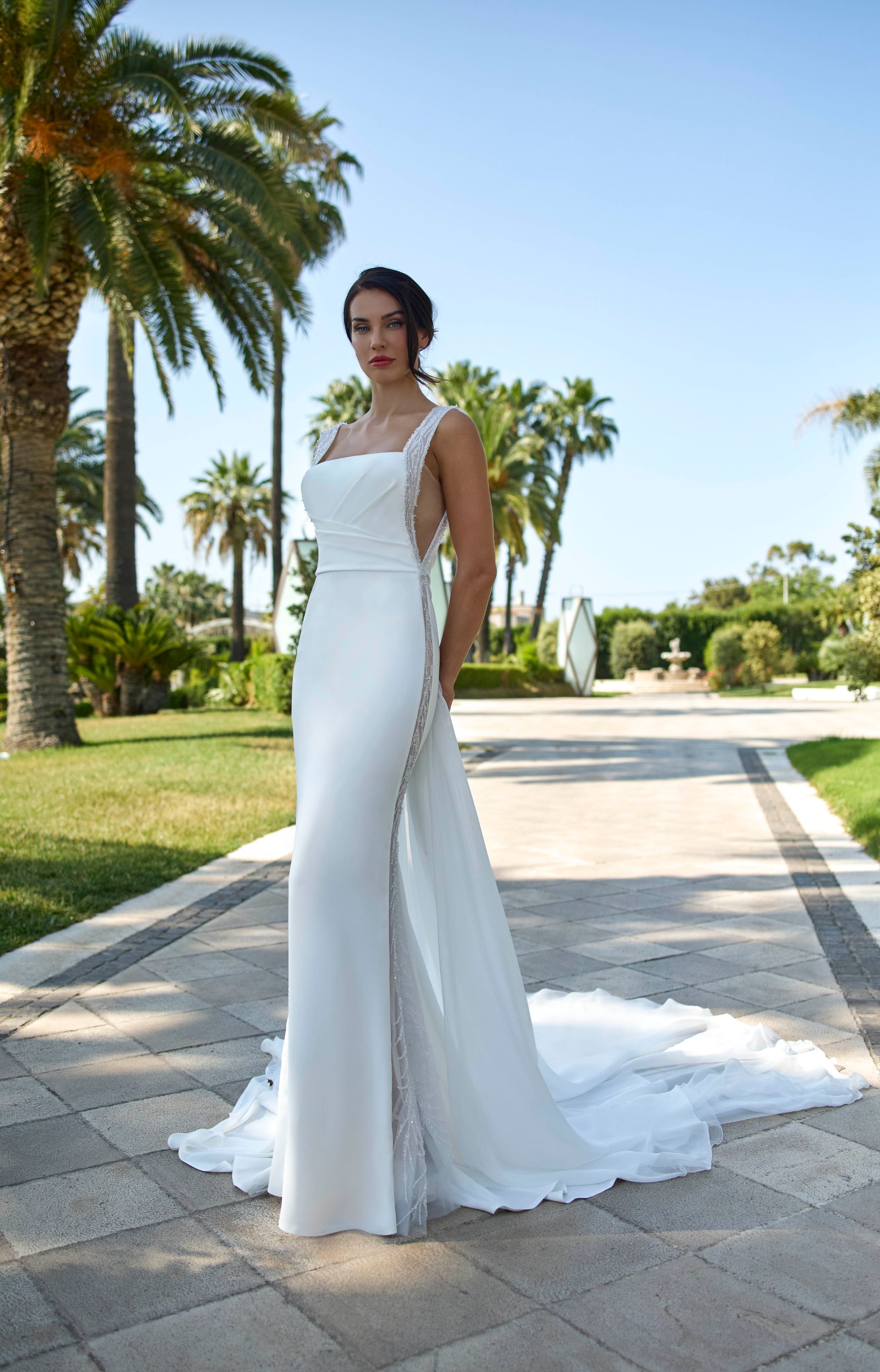 Donna in abito da sposa bianco con strascico in piedi sul sentiero, all'aperto.