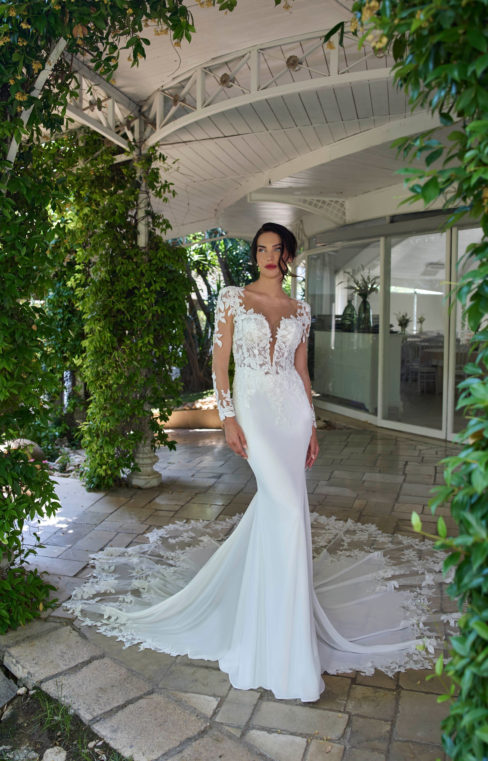 Una donna in abito da sposa bianco con lungo strascico posa all'aperto.