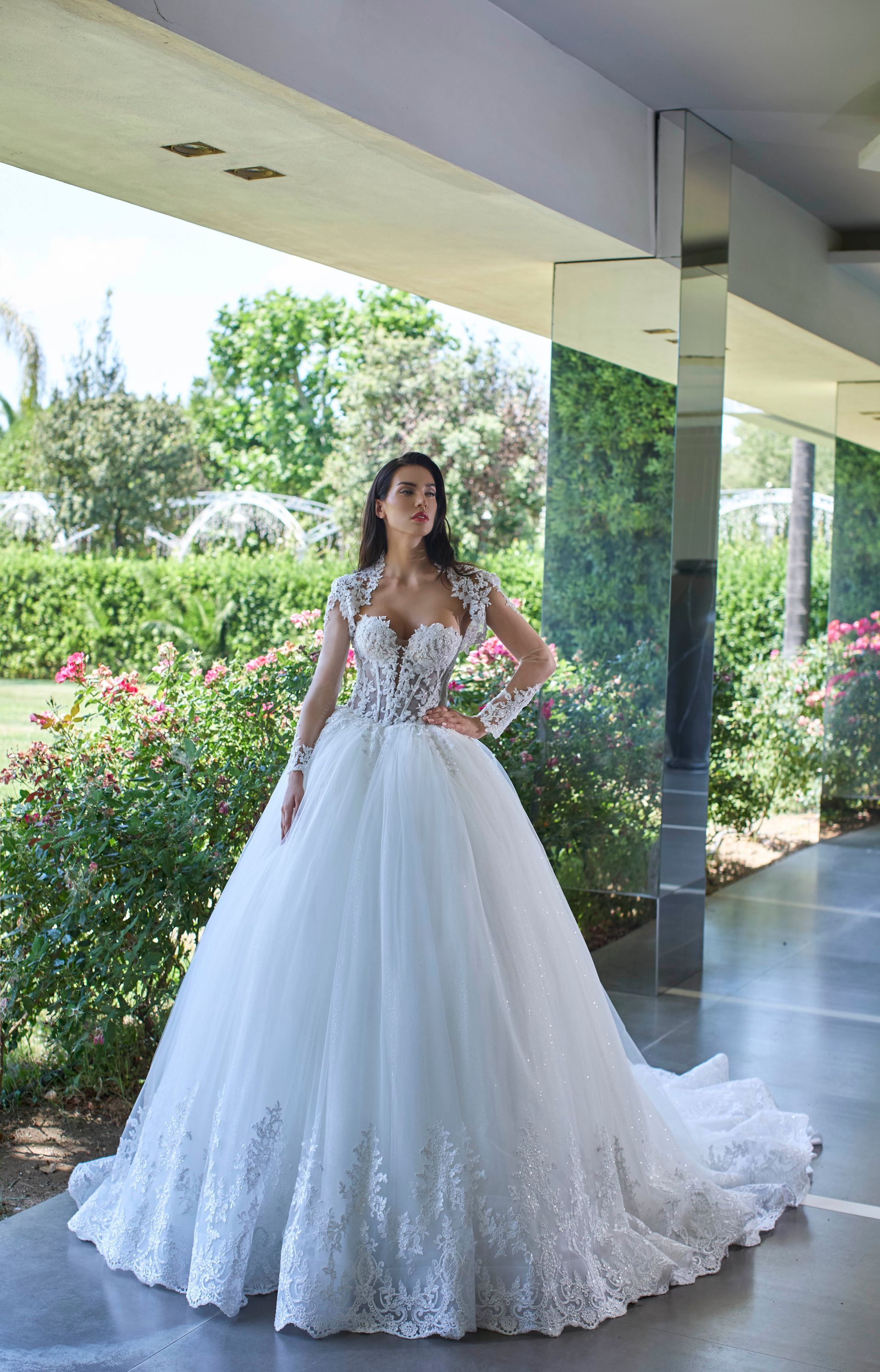 Donna sorridente in abito da sposa bianco, in piedi fuori da un edificio con composizioni floreali.