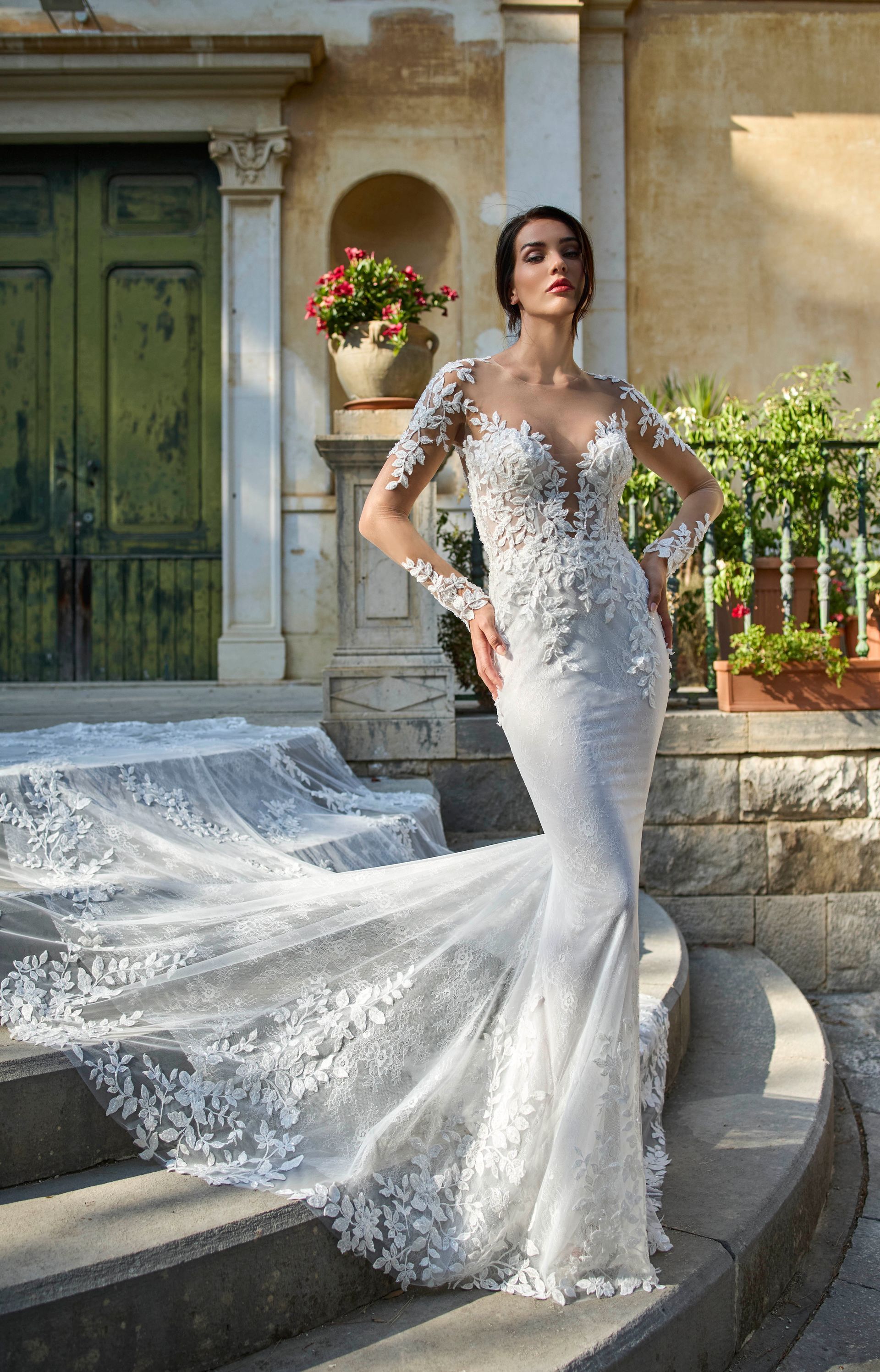 Una donna in abito da sposa in pizzo bianco con lungo strascico posa sui gradini di pietra.