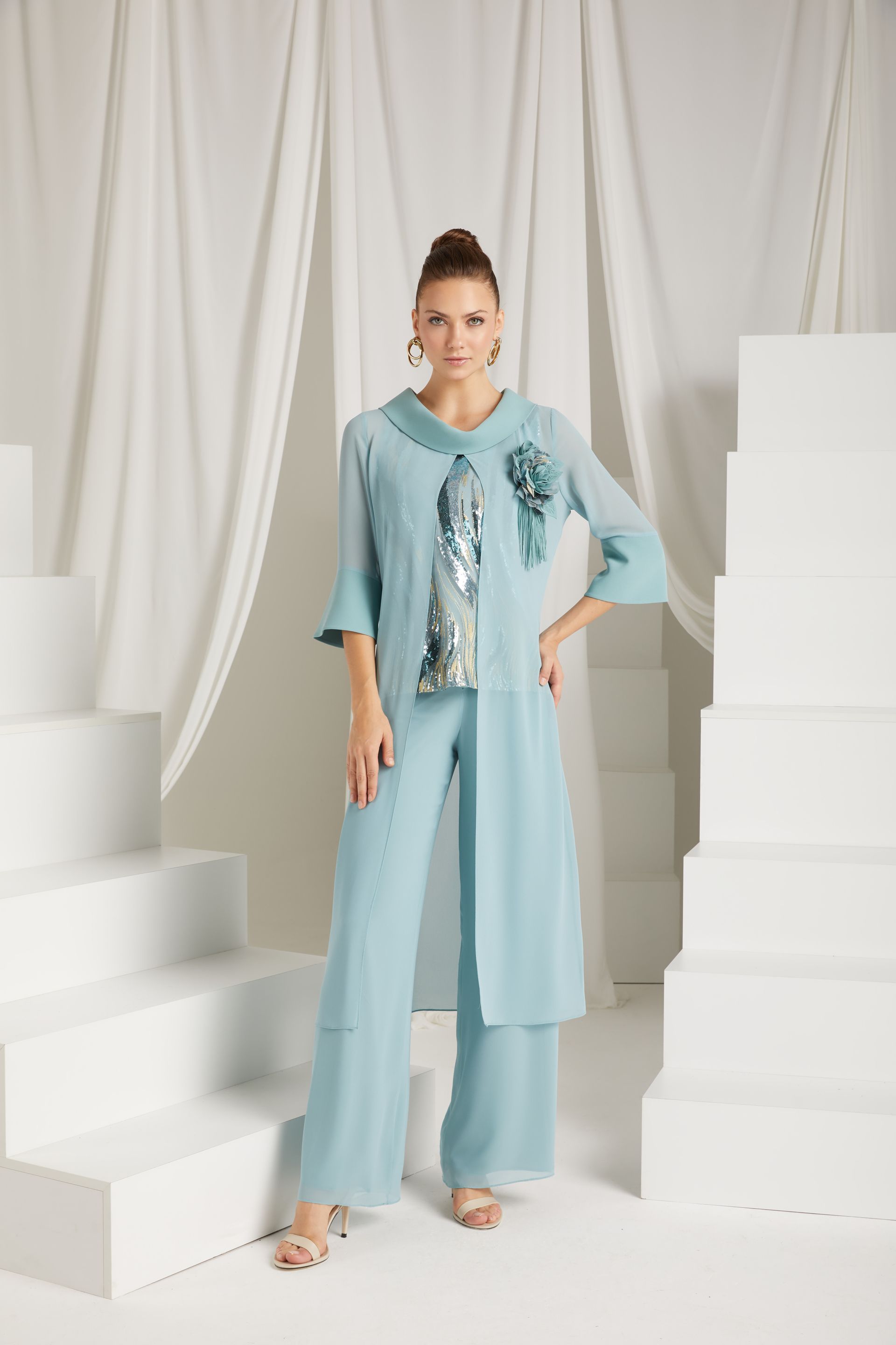 Donna in tailleur azzurro, in piedi su una scala bianca, con le braccia sui fianchi.