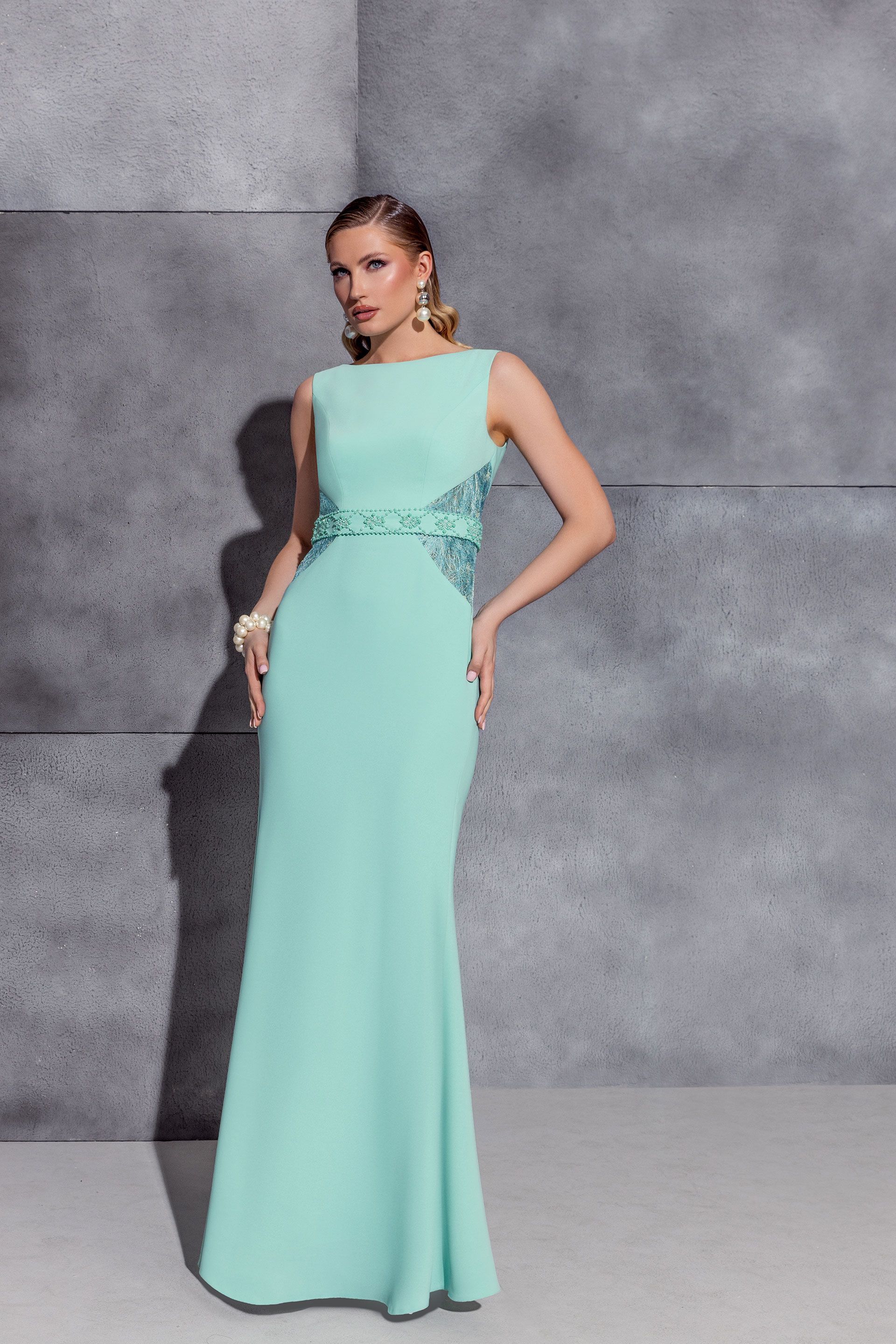 Una donna in abito formale verde menta posa contro una parete grigia testurizzata.