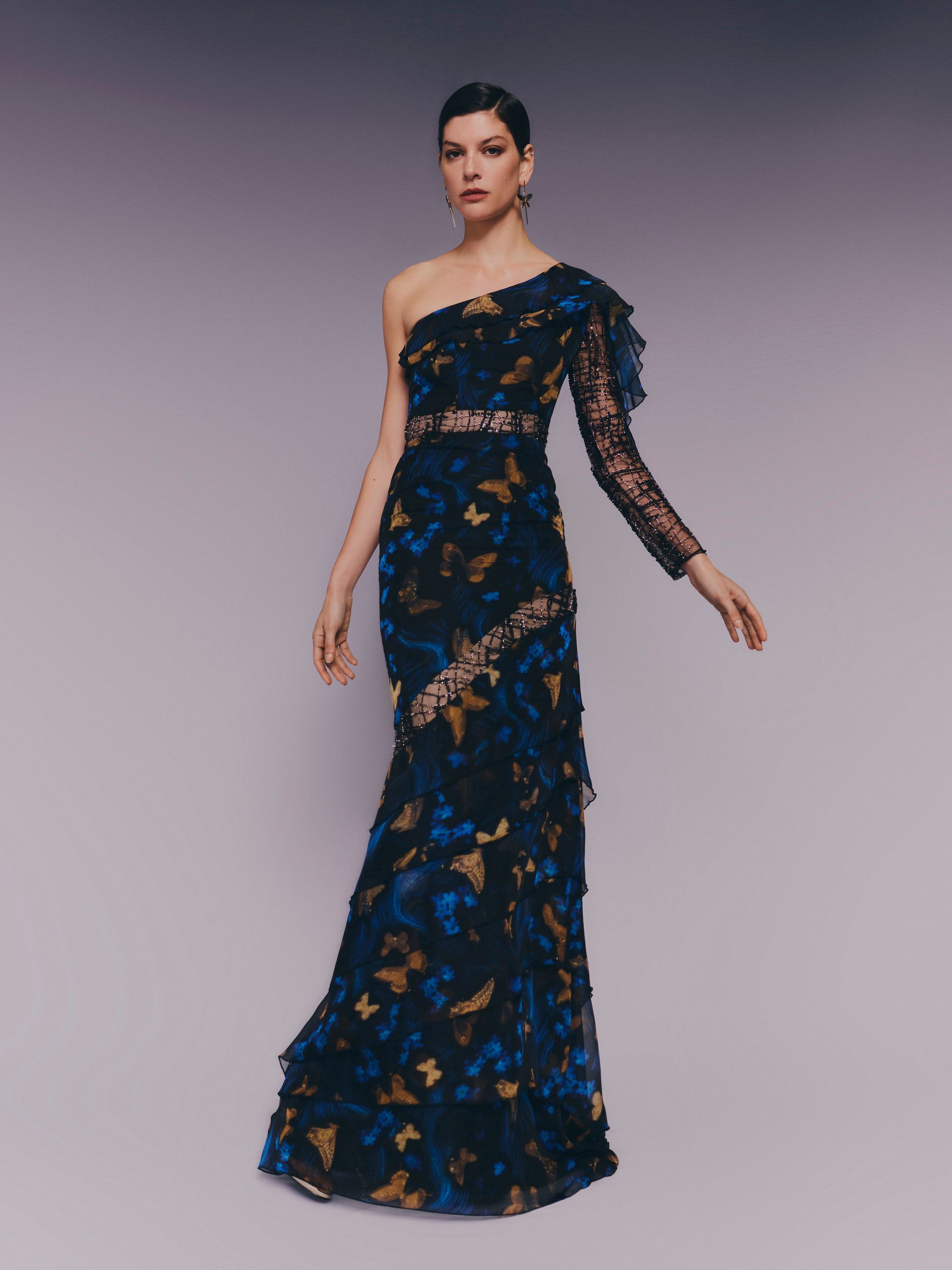 Donna in abito da sera monospalla decorato, in posa su uno sfondo grigio.