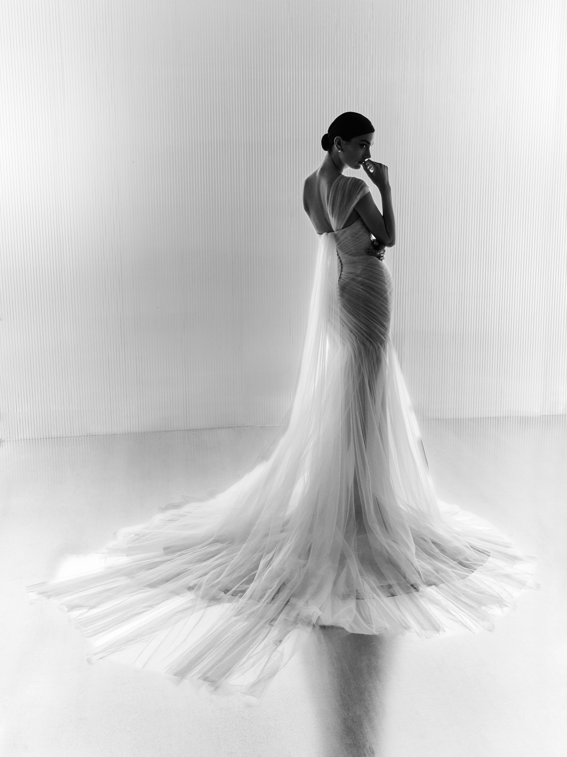 Donna in abito da sposa bianco, di spalle all'osservatore, in piedi su una superficie riflettente.